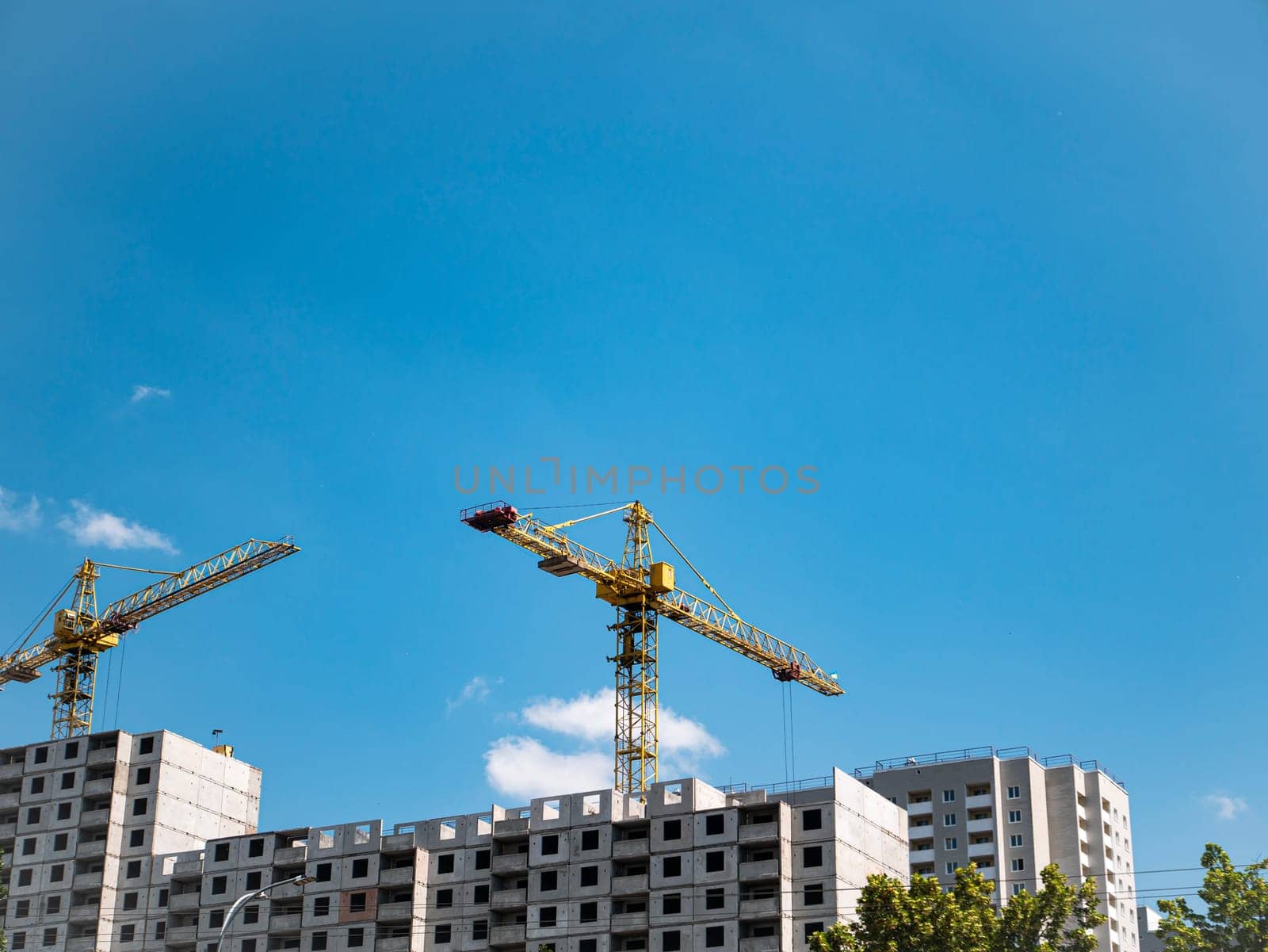 House construction with construction cranes on a background of blue sky. Construction and repair. Industry. Building sector. Poster. Advertising. Place for text. Template. Background image.