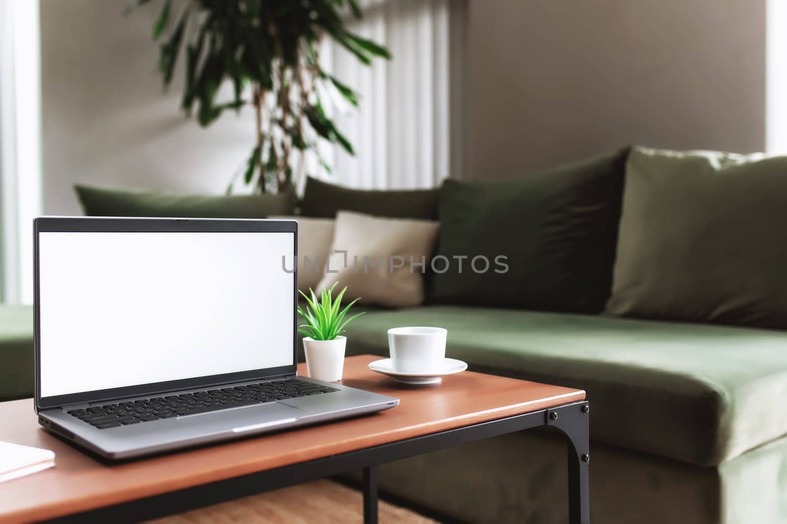 Work from home, workspace, desktop, remote work concept, gray laptop computer with empty white screen mock up on brown wooden table with white cup of coffee, note pad, flowerpot, blurred background