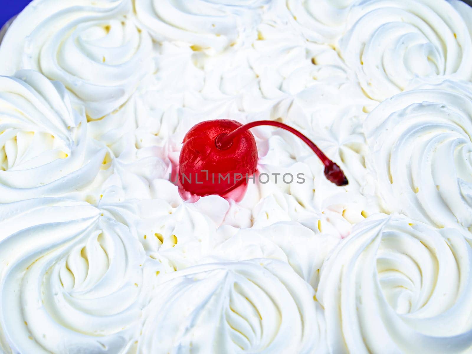 Red cherry from marmalade on white creamy flowers of a biscuit cake. Food photo. Dessert. Cake baking. Place for text. Shop window. Poster. Promotional event. Cake recipe.