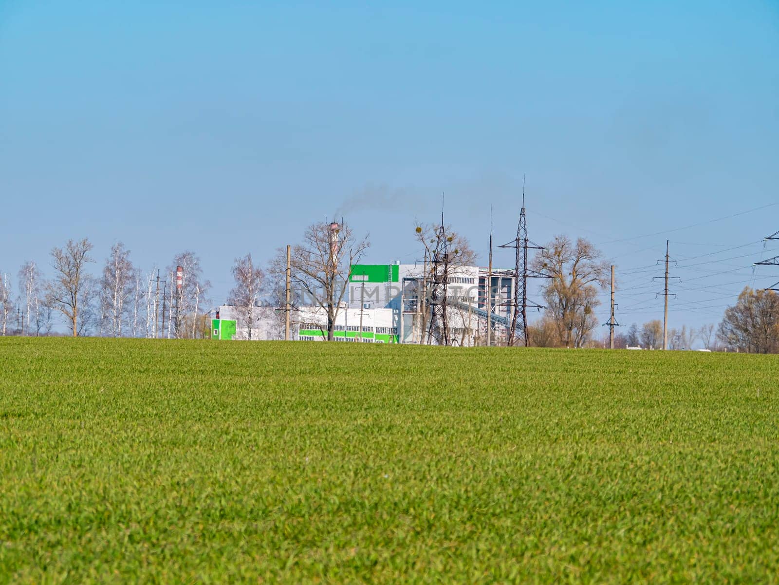 Industrial plant on a green field horizon of a farm. Cloud horizon. Agriculture. Place for text. Background image.