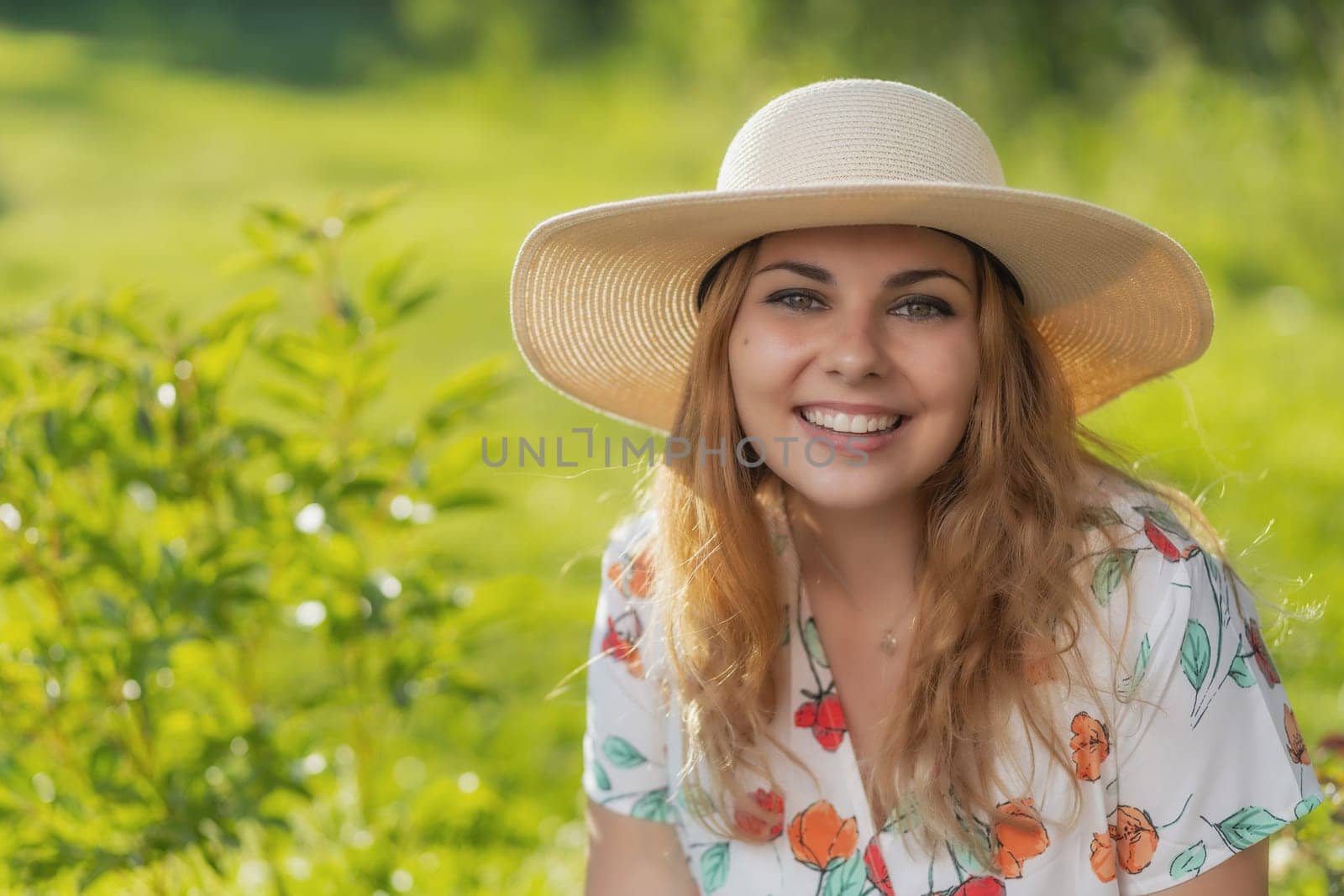 Smiling attractive  young woman wearing straw hat is posing outdoors. Horizontally.