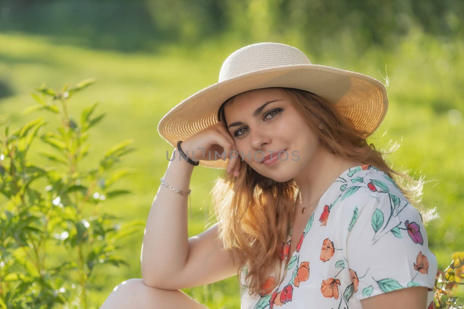 Cool young woman wearing straw hat is posing outdoors in summer day. Horizontally.