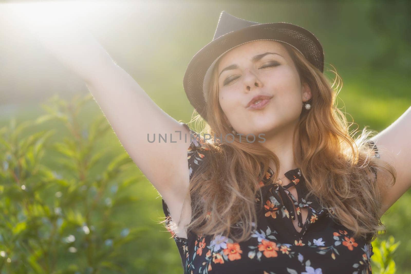 Attractive young girl wearing a hat enjoying with outstretched arms in the backlight. Horizontally.