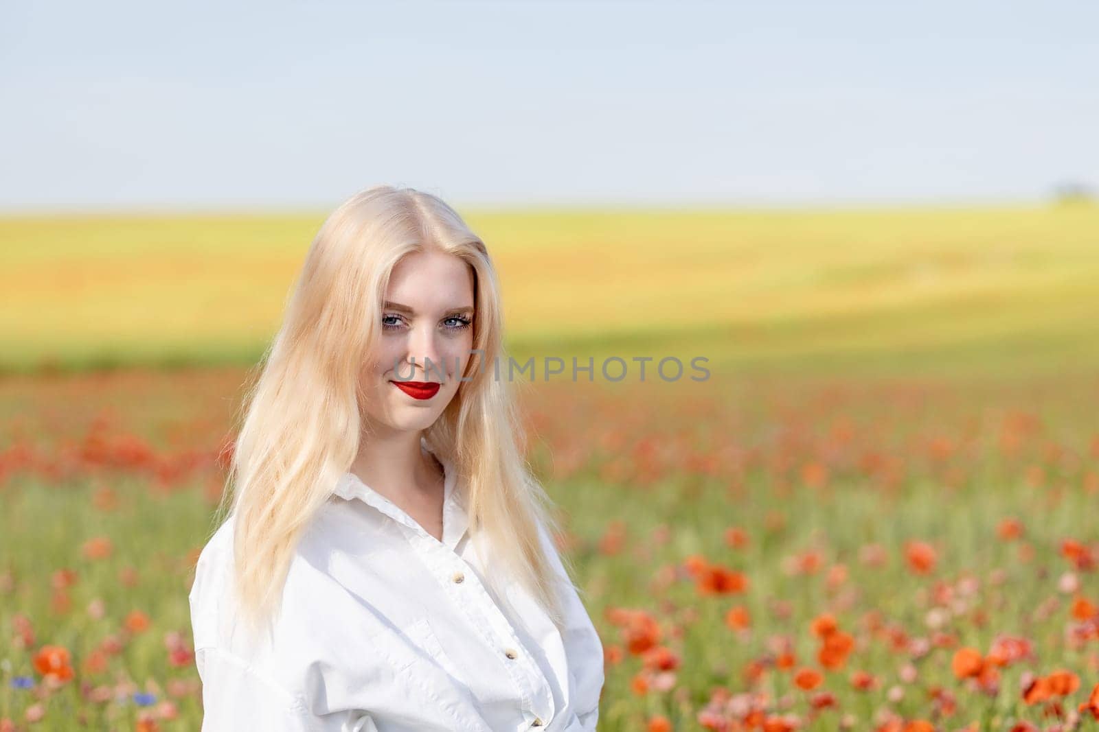 Smiling blonde girl is  posing in red poppy field.  Horizontally.