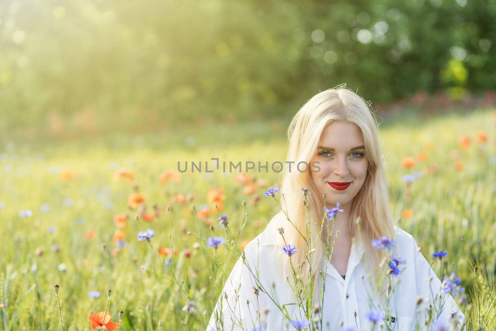 Blonde young woman posing in summer flower meadow.  Horizontally.