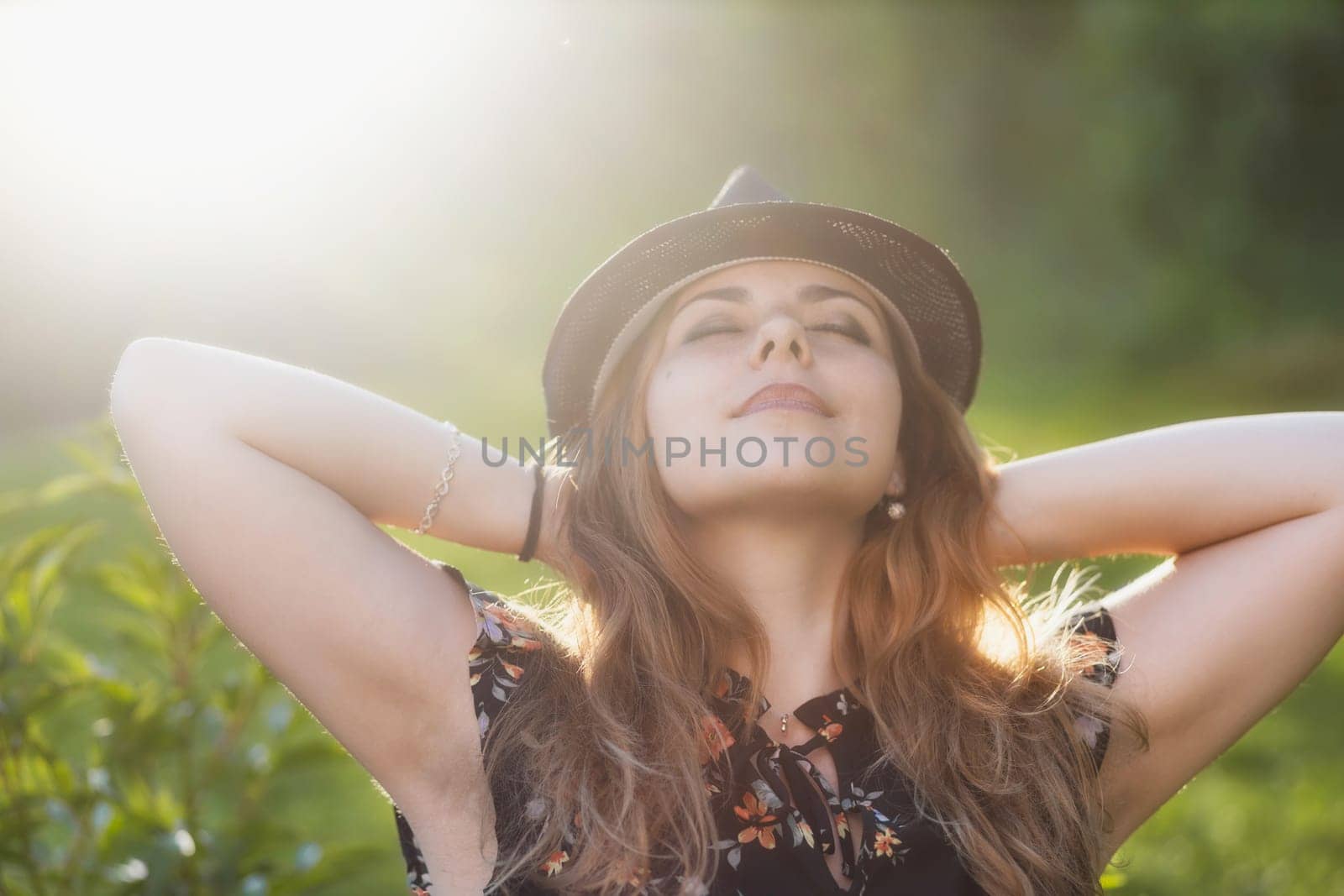 Attractive young girl wearing a hat enjoys with her hands behind her head. Horizontally.