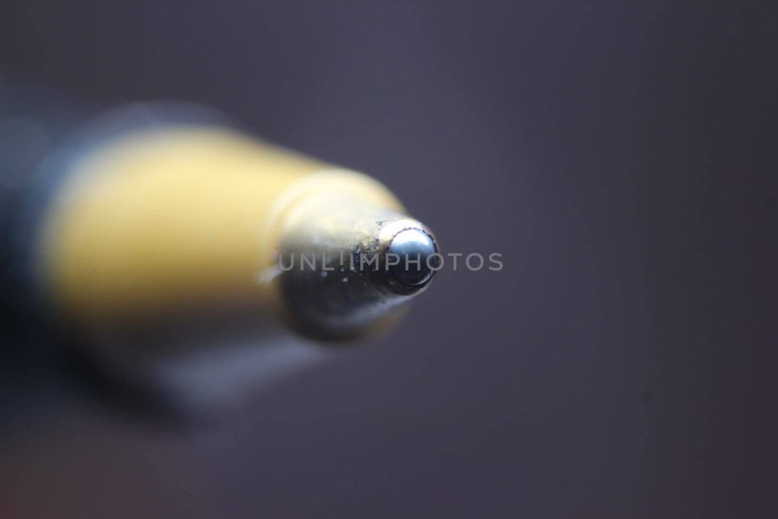 Macro photo of ballpoint pen tip with dark grey background. Extreme macro image of metal ballpoint pen on grey background.