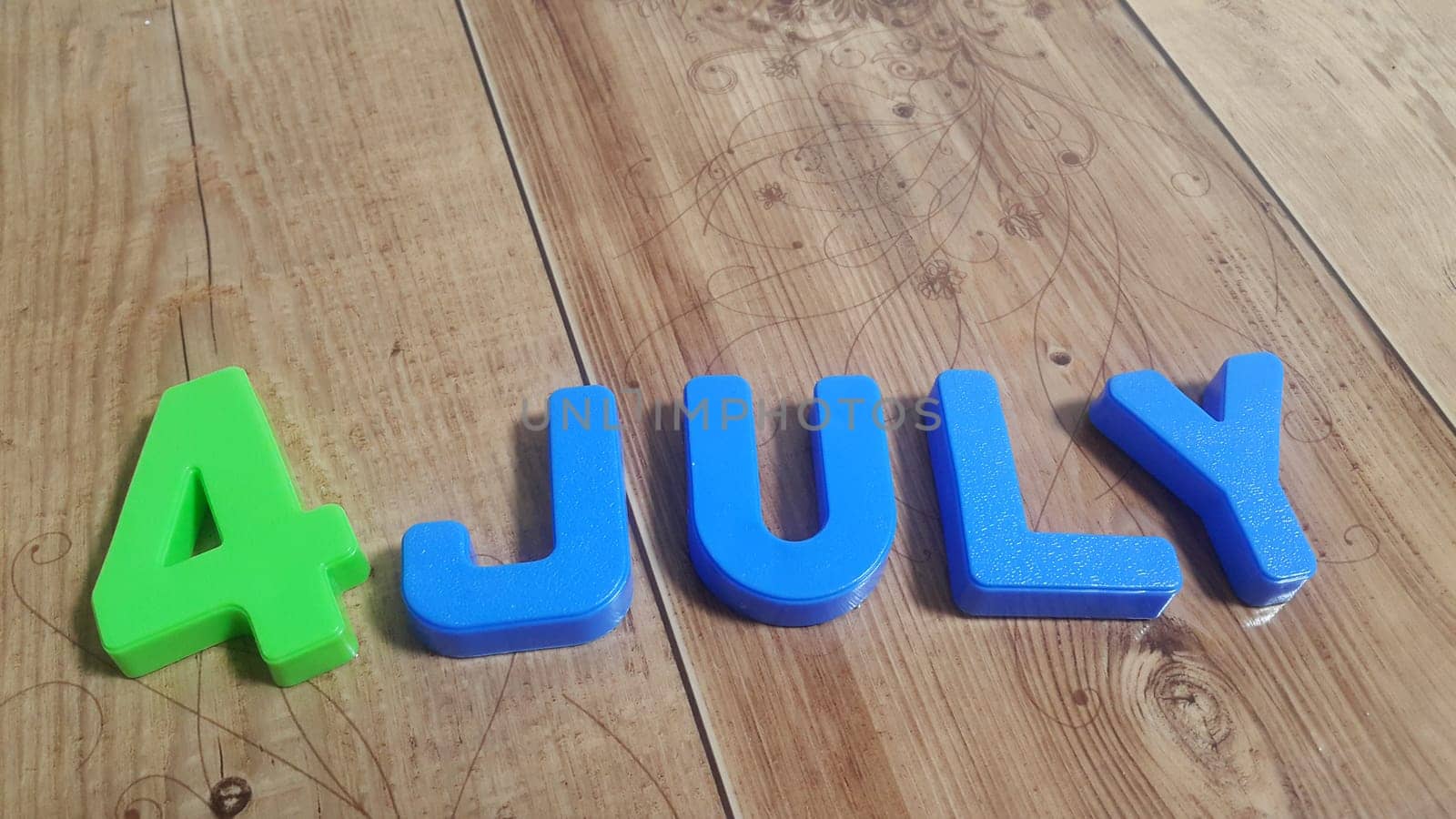 Plastic colored alphabets making words 4 july are placed on a wooden floor. These plastic letters can be used for teaching kids.