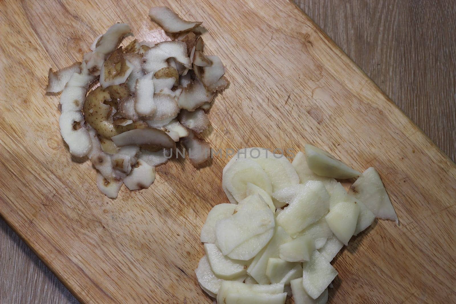 Chopped potato slices with peelings on a wooden cutting board