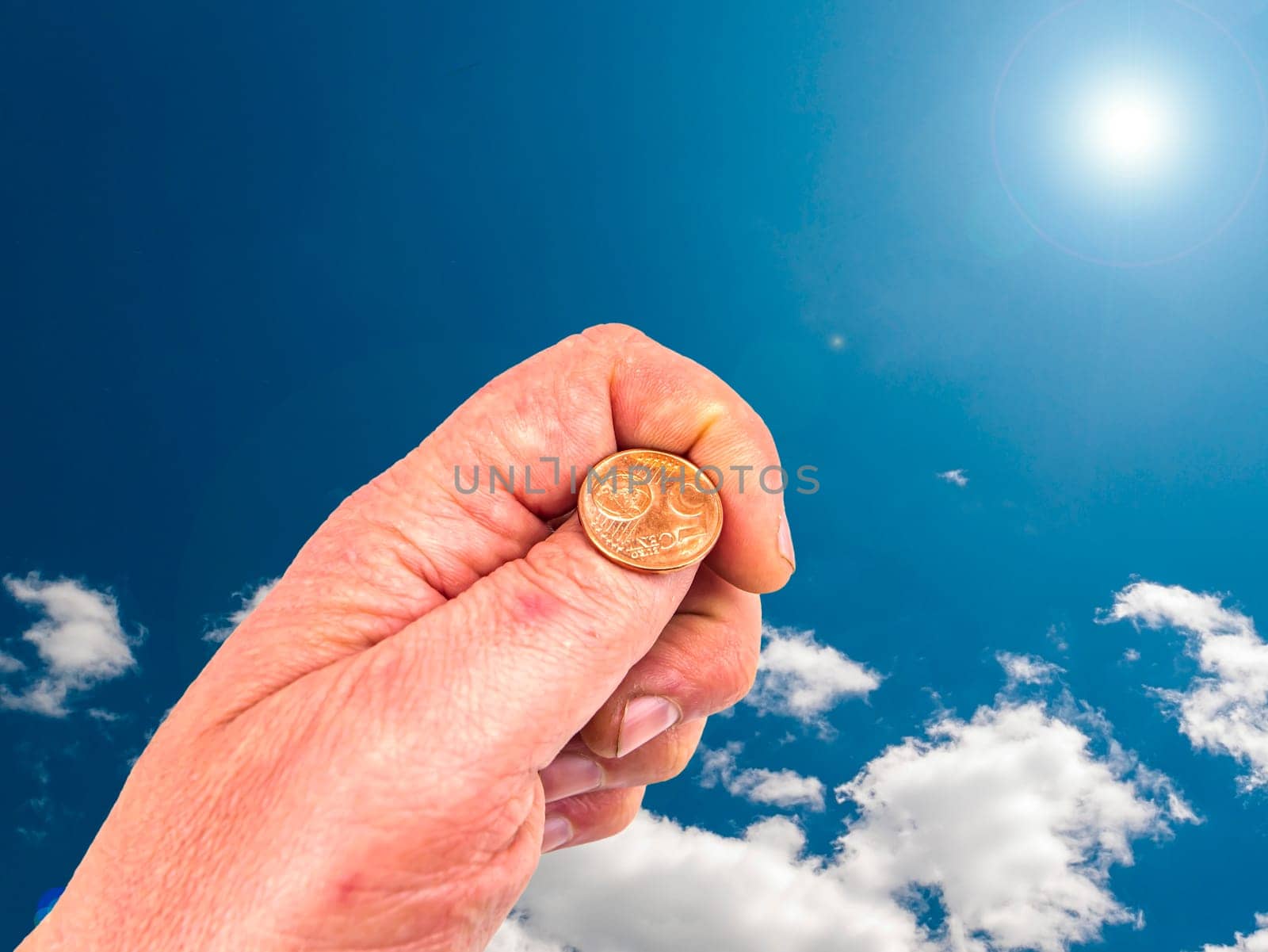 Hand with coins on a background of blue sky. God's gift. Prayer. Request for help. They ask for money. Cast lots. The hand of the giver. Sunbeams. Euro money. The image is in the background.