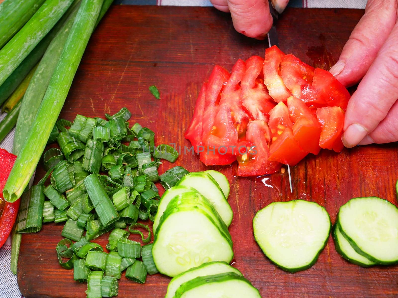 Slicing a red tomato with a knife on a cutting board. Green vegetable salad. Cook. Home kitchen. Vegetarian food. Recipe. Promotional photo. Hands of a man. Vitamins