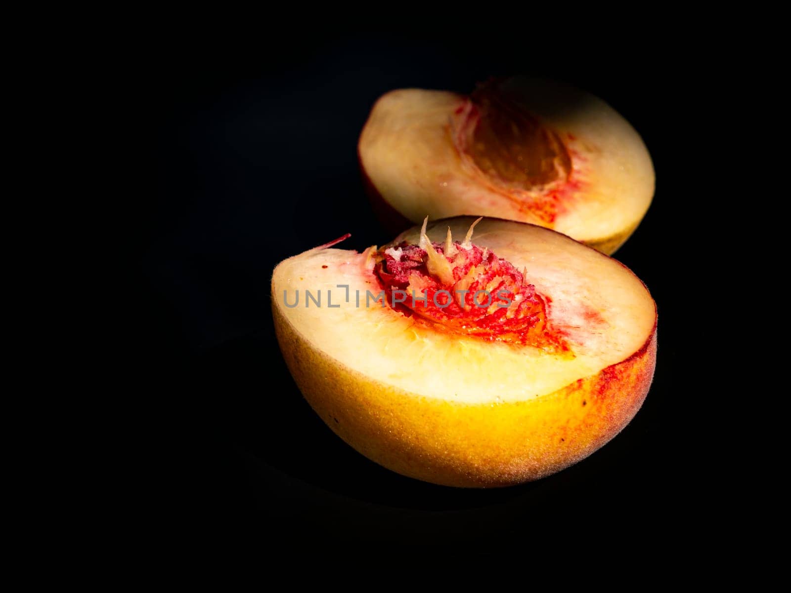 Half peach fruit on a black background. Peach bone. Food photo. Harvesting. Peach juice. Agriculture. Advertising photo of a shop window of a fruit shop. Place for your text. Background image.