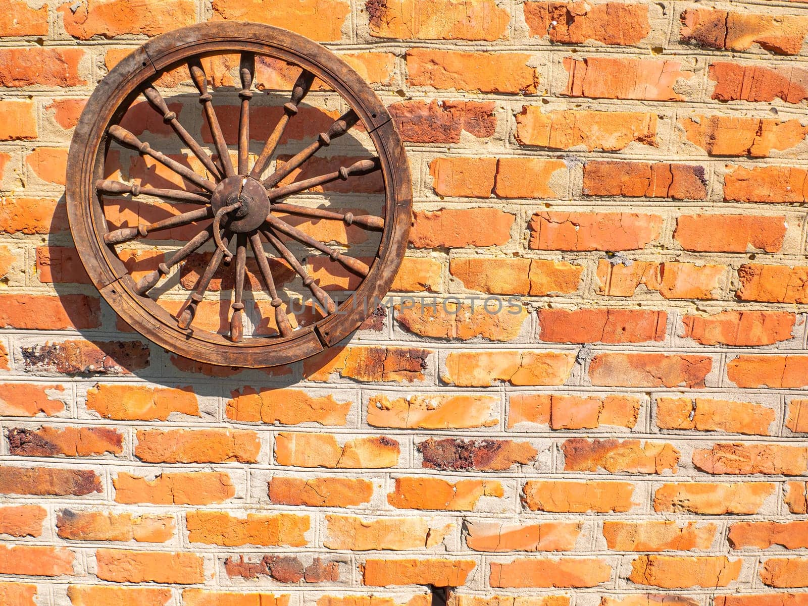 Old wooden wheel on a brick wall. Wooden wheel of a horse carriage. Red brick wall. Decor element. Retro style. Background image. Place for your text.