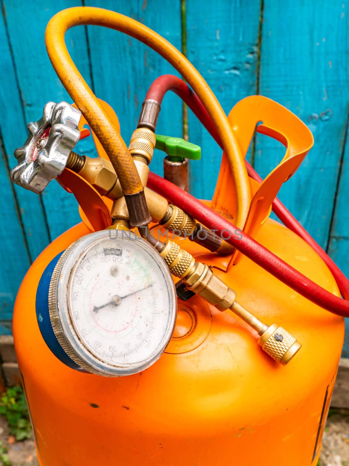 Refrigerant cylinder and hoses with pressure gauge. Orange bottle with freon. Pressure gauge for the repair of refrigerators and air conditioners. Refrigerator and air conditioner repair tool.