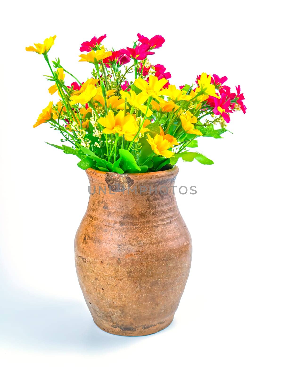 A bouquet of artificial flowers in a clay jug. Bouquet of pink and yellow flowers. Ceramic vase. Earthenware. Handmade. White background. Background image. Place for your text.