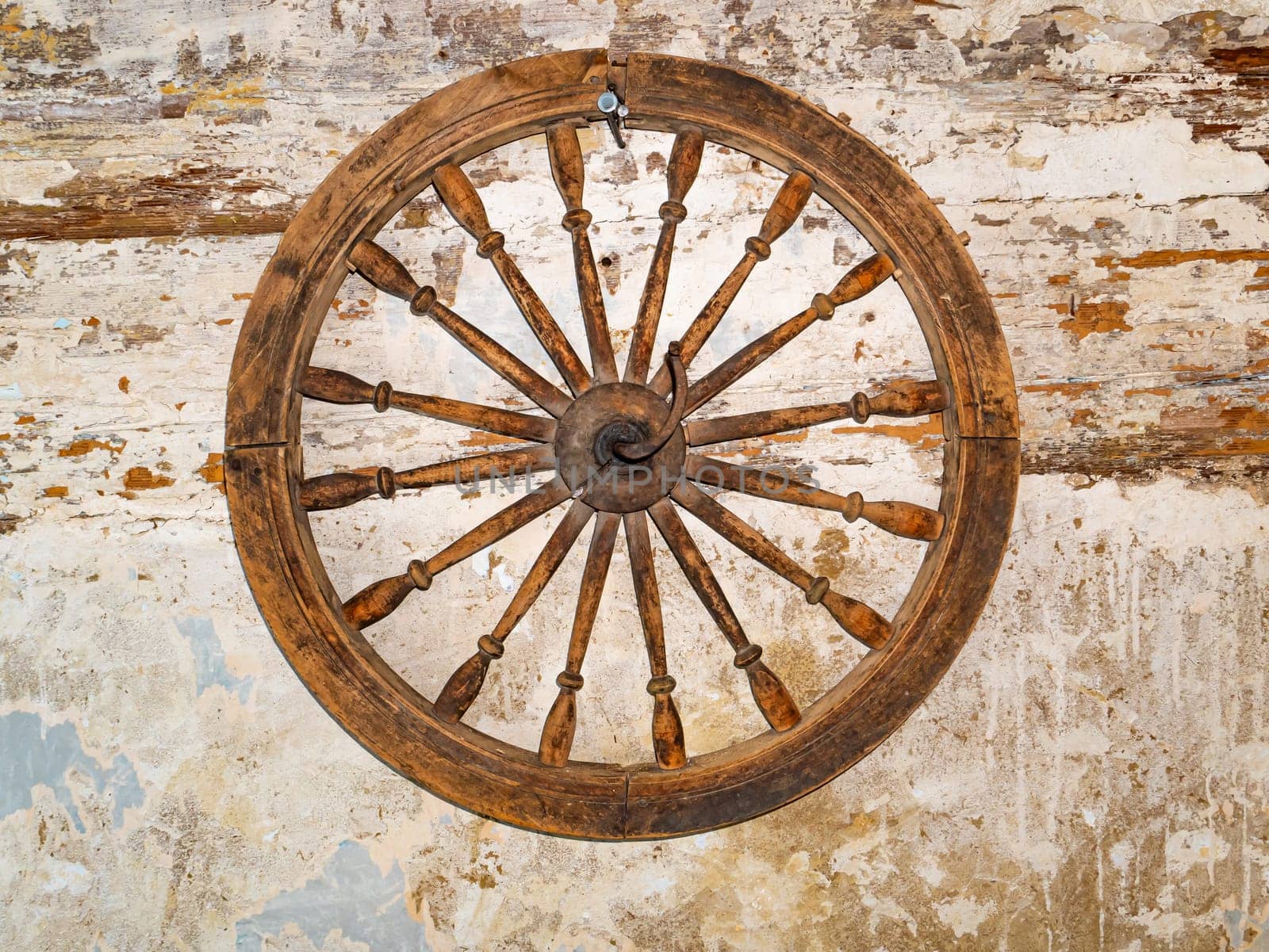Wooden wheel on an old shabby wall. Wooden cart wheel. Retro room interior. Old-fashioned background. Background image. Place for text.
