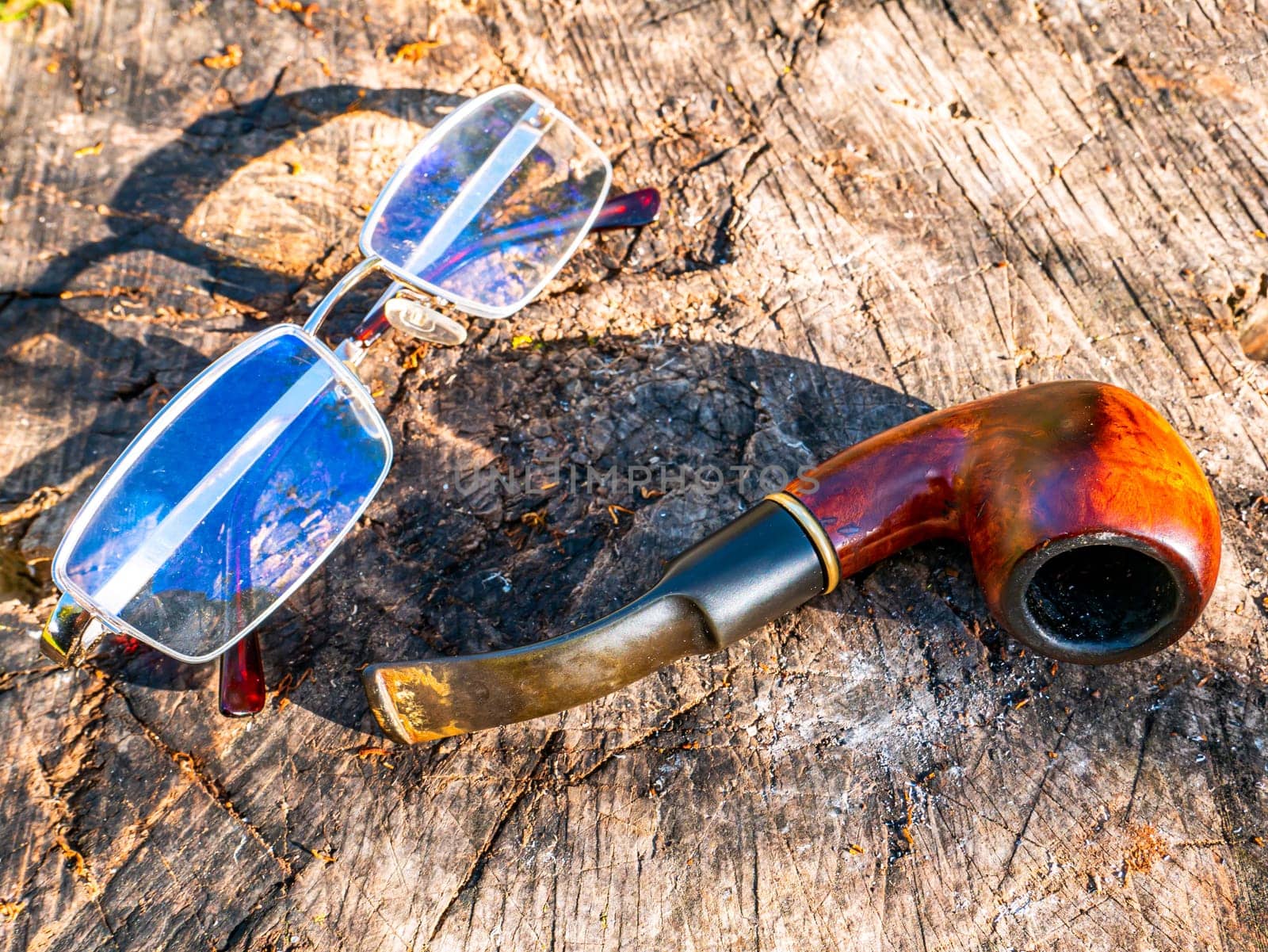 Smoking pipe for tobacco and glasses on a wooden table. Wooden pipe for smoking tobacco. Smoker's tool. Bad habits. Nicotine addiction. Nicotine in cigarettes. Place for your text. Background.