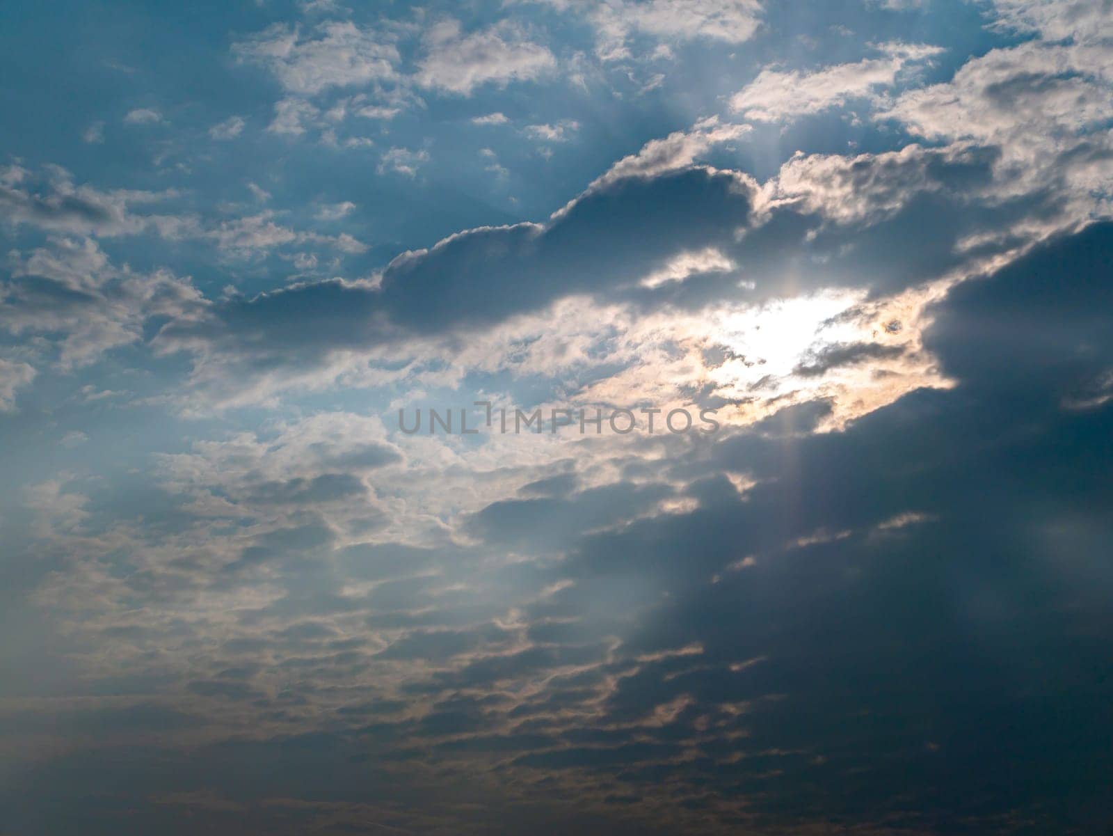 Orange rays of sunset through storm clouds. Yellow evening dawn. Morning yellow sunny dawn. Clouds in the blue sky. orange morning dawn. Heavenly landscape. Space. Stratosphere.