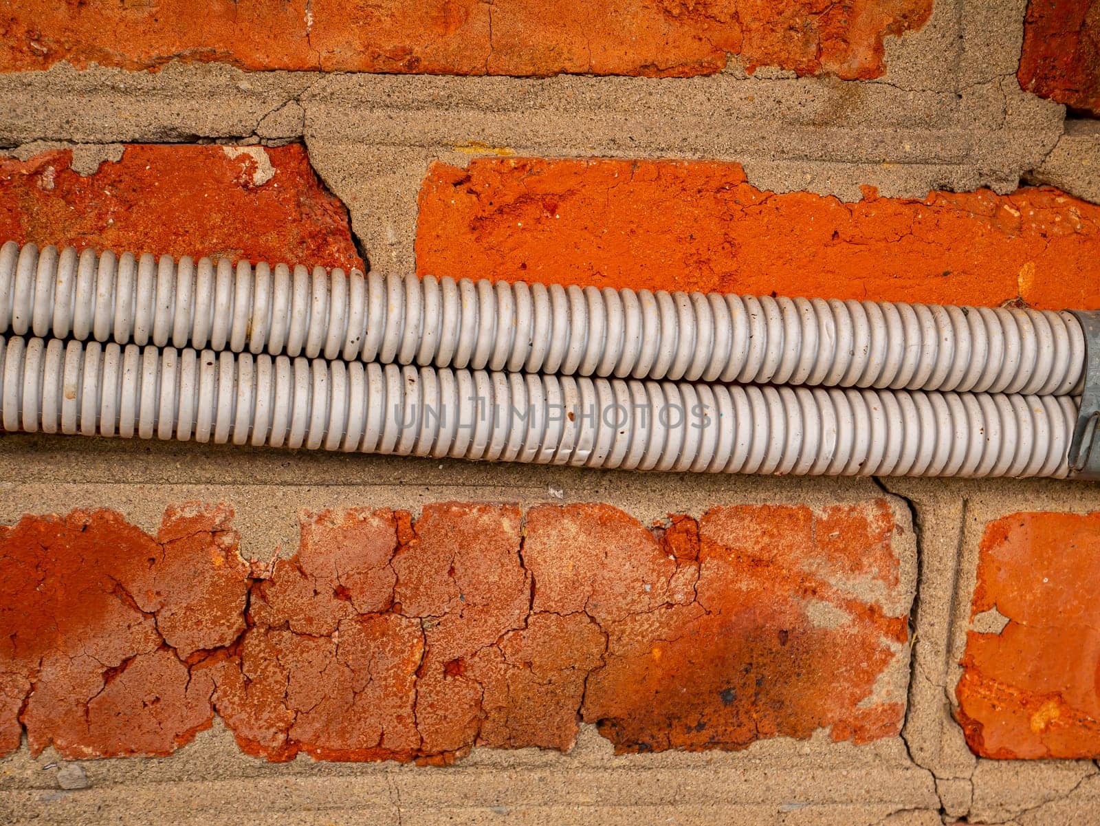 Electrical wiring in plastic corrugation on a brick wall. Electrical wiring. Corrugation for wires. Master electrician. Electrician repairman. Volt. Ampere. Watt. Red brick wall. Place for text.