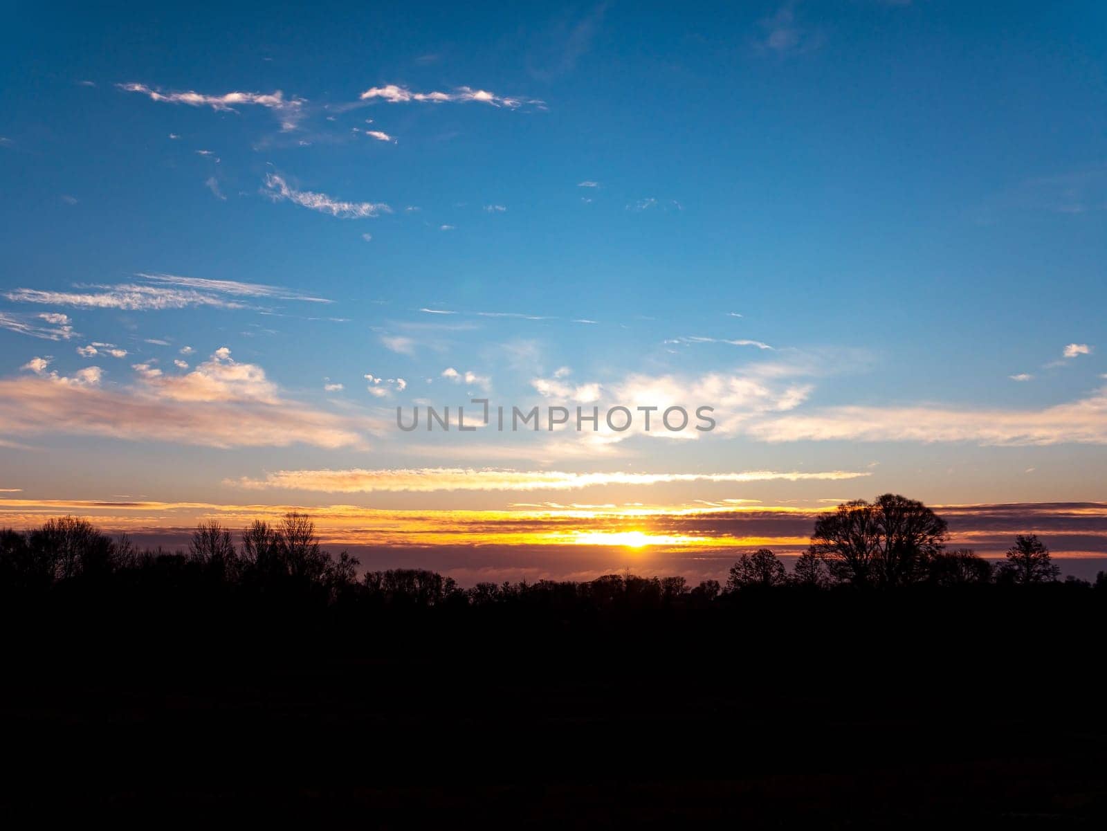 Morning sunrise on the horizon with clouds. Morning dawn. Evening sunset. Evening time of the day. Cloudy horizon. Shadows of trees. Natural landscape. Blue sky with clouds. Day and night. Scenery.