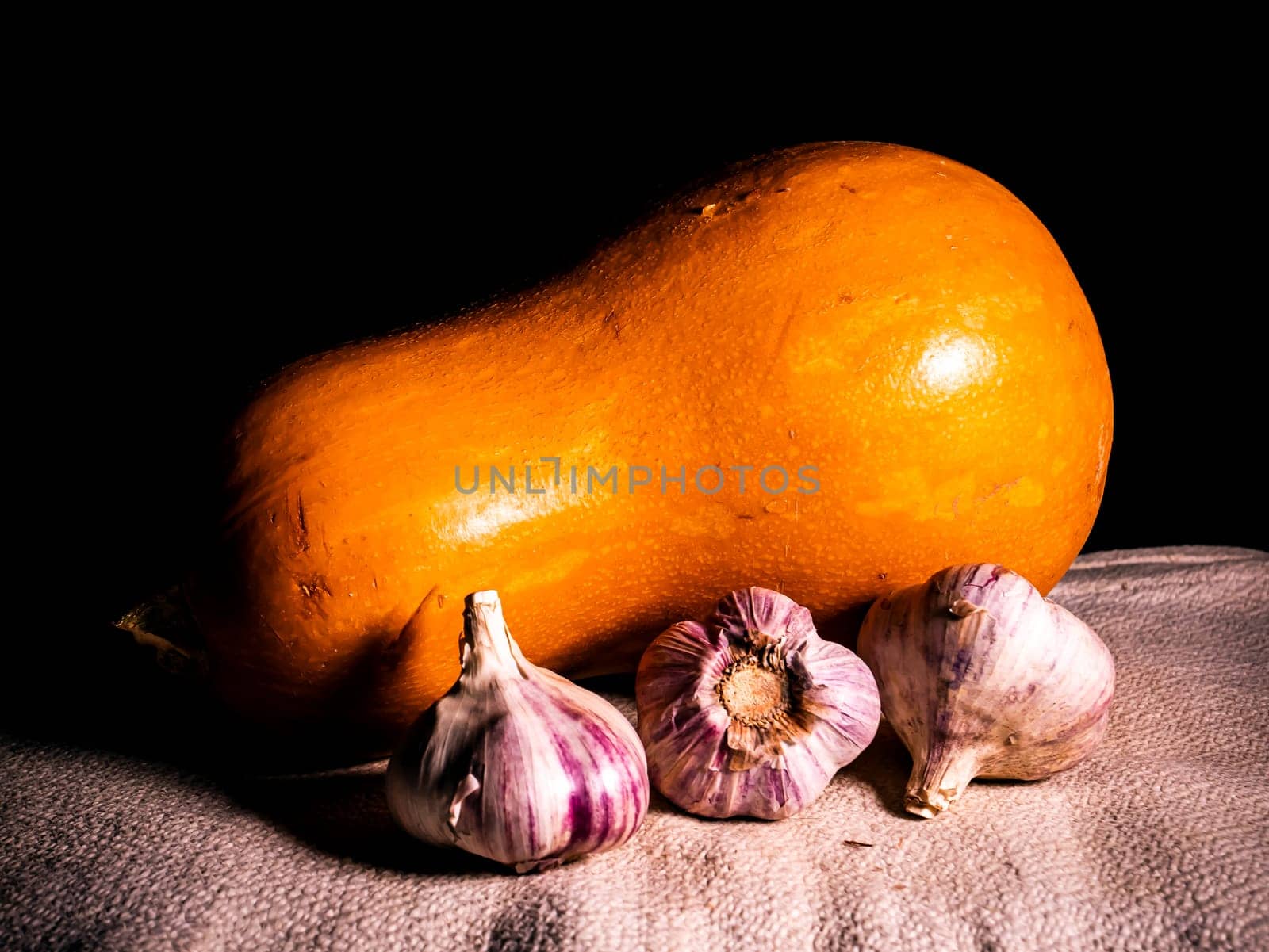 Orange pumpkin and garlic vegetable on a black background. Harvest vegetables. Head of garlic. Halloween orange pumpkin. Halloween holiday. Agriculture. Background image. Food photo.