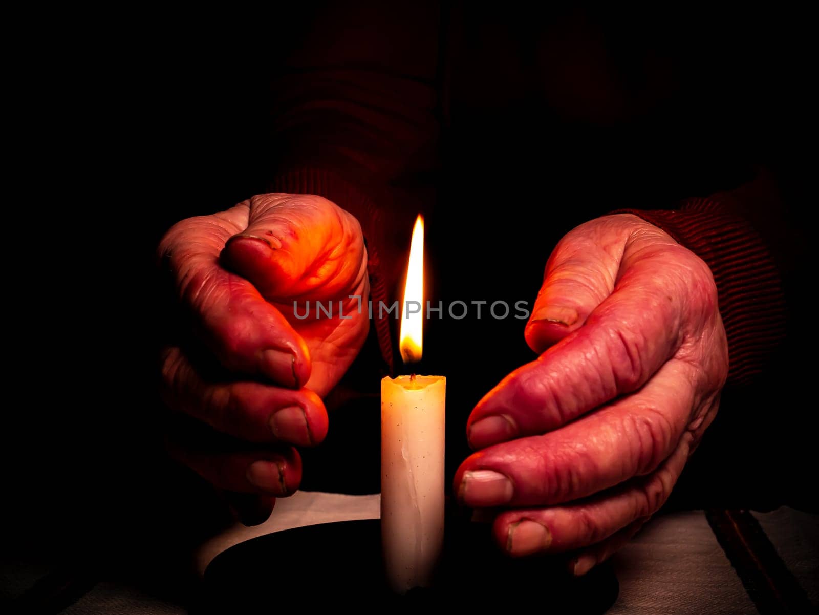 The flame of a burning wax candle in the hands of an old man. The flame of a wax candle. Fire in the dark. Day of Remembrance. A minute of silence. Funeral services. Sorrows on Memorial Day.