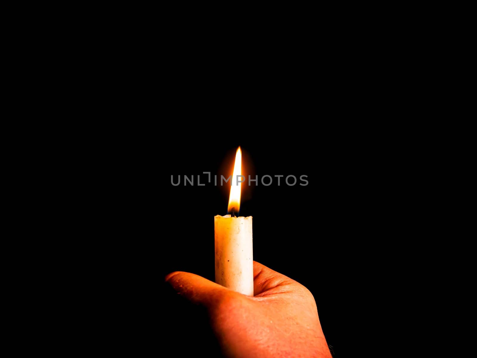 The flame of a burning wax candle in the hands of a man. The flame of a wax candle. Fire in the dark. Day of Remembrance. A minute of silence. Funeral services. Sorrows on Memorial Day. Night.