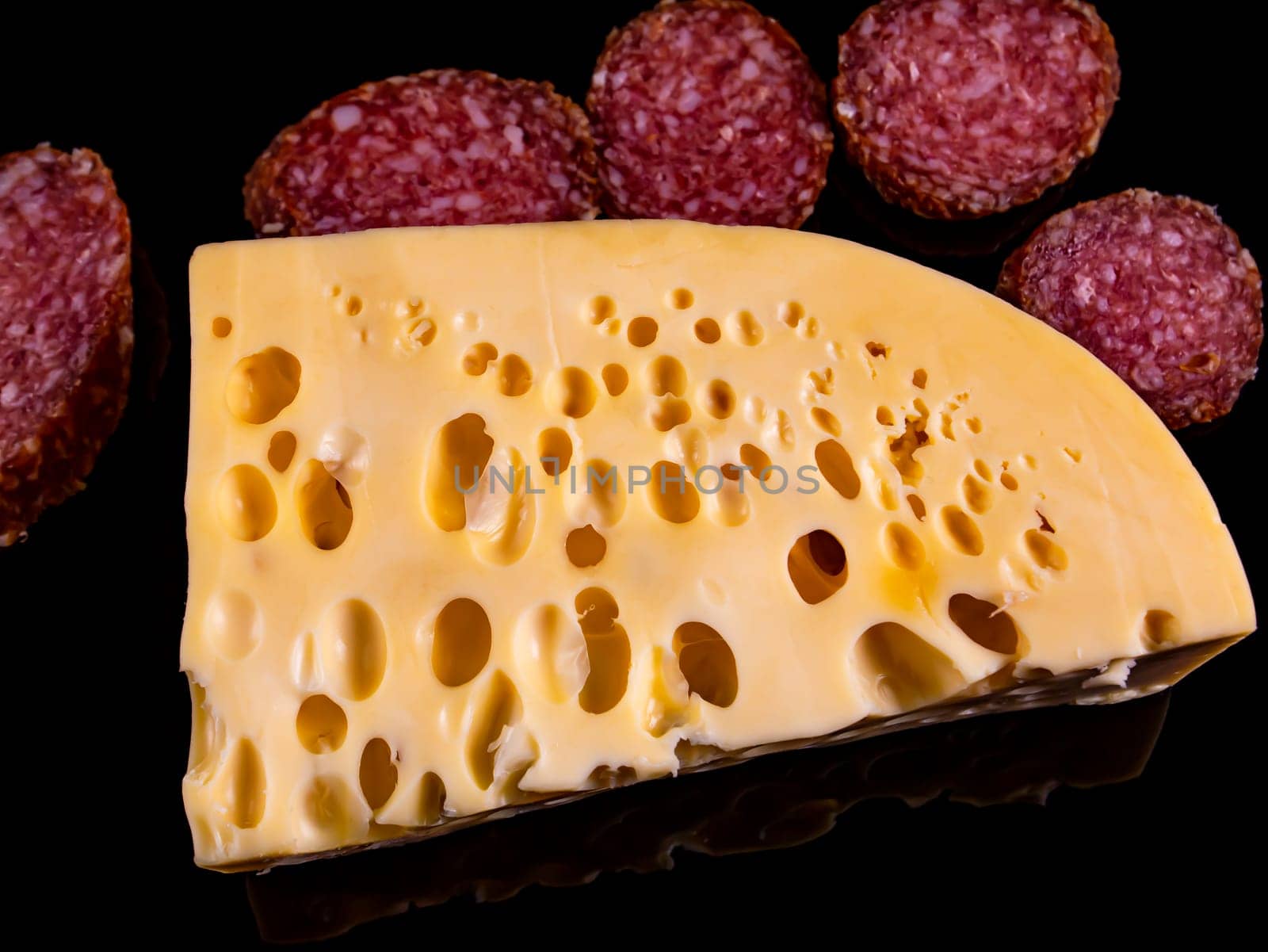 A piece of hard cheese and a sliced sausage on a black background. Hard cheeses. Meat sausage. Milk product. Meat sausages. Dairy products. Home kitchen. Food photo. Black background.