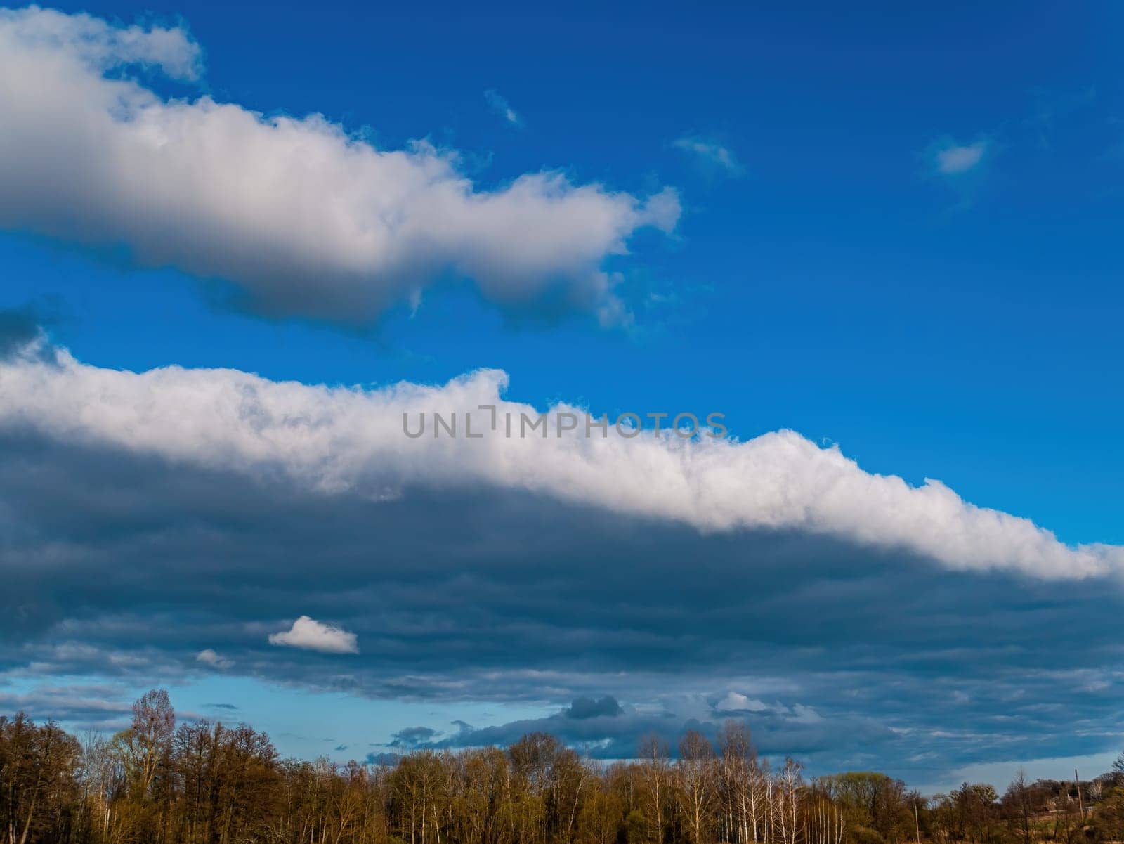 Forest horizon against a blue sky with white clouds. Cloudy horizon. Blue sky. Forests and meadows. Natural season. Spring season. Rain clouds. Background image.