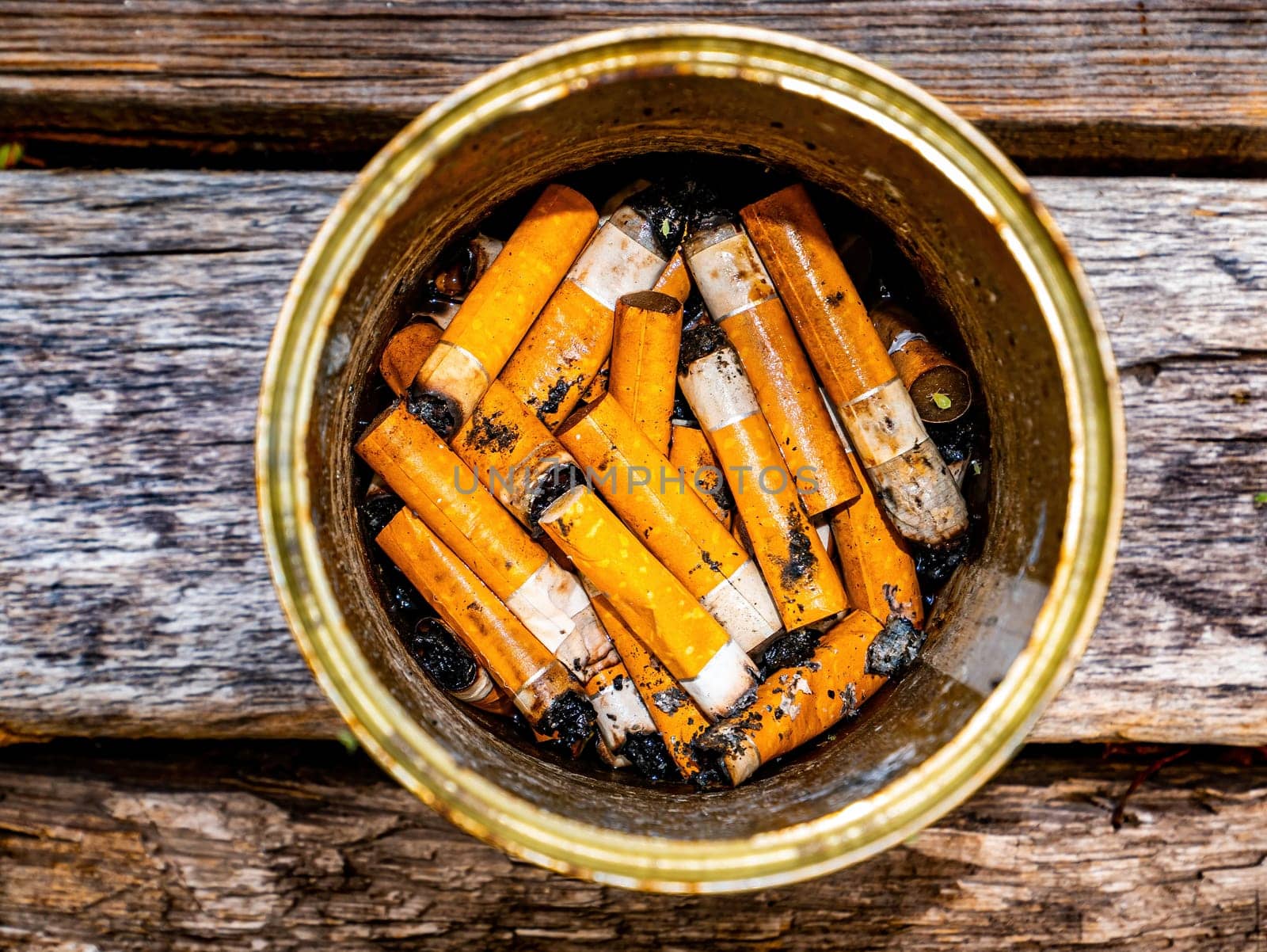 Ashtray from a tin can with cigarette butts on a wooden table. Tin can. Ashtray for cigarette butts. Smoking area. Smoker. Drug addiction. Not a healthy lifestyle. Nicotine and tobacco.