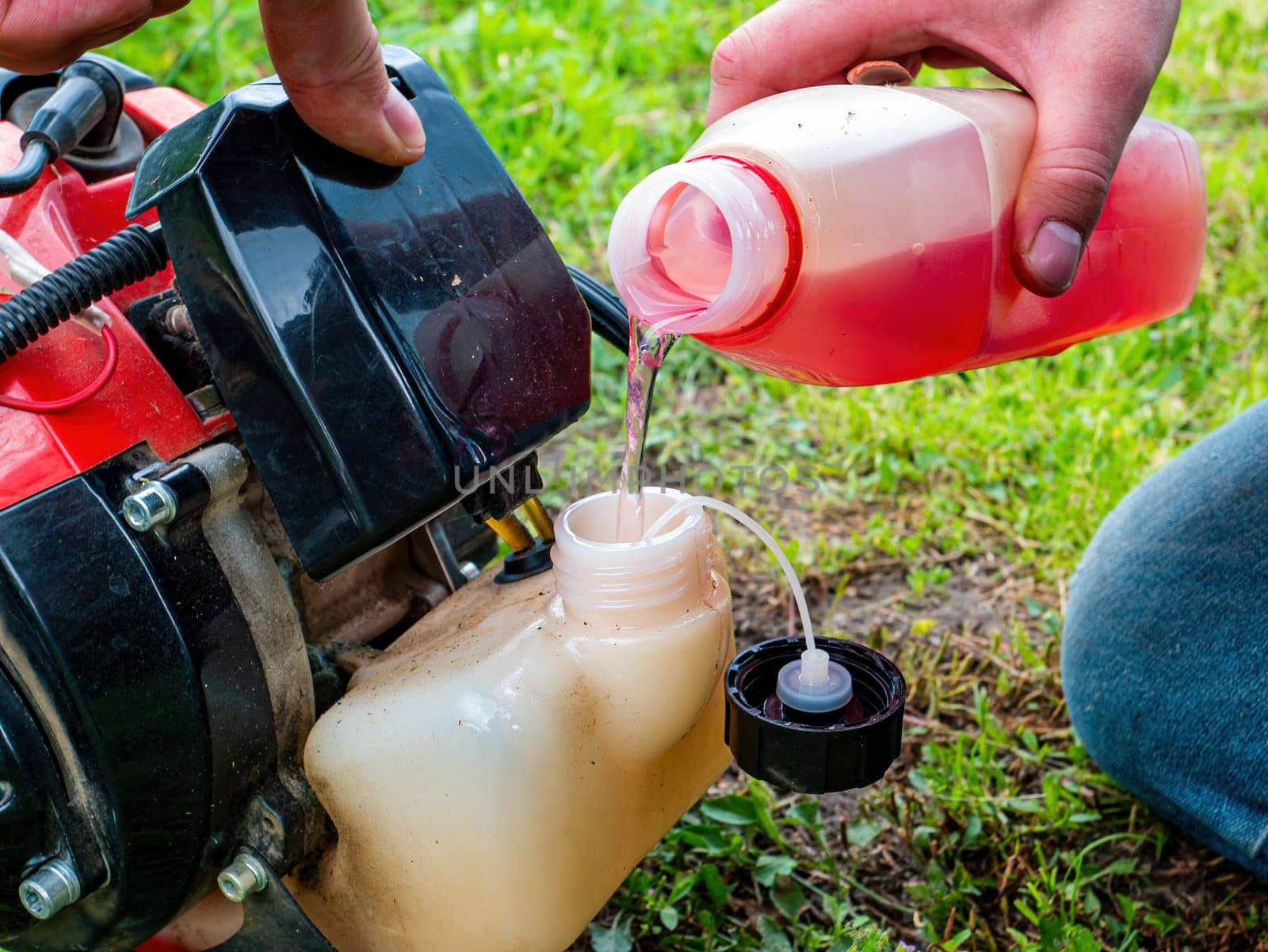 Refueling a petrol-powered lawn mower. A grass trimmer. Gasoline fuel. Fuel tank. The working process. Gardening equipment. Gardening Tools. Industrial equipment.