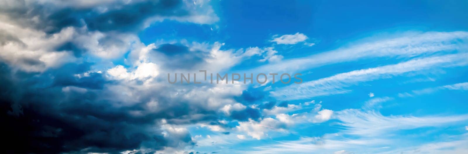 Thundercloud against a blue sky with white clouds. Cloudy blue sky. Approaching a thunderstorm cyclone. Space. Sunlight. Panoramic photo. Weather forecast. Natural landscape.