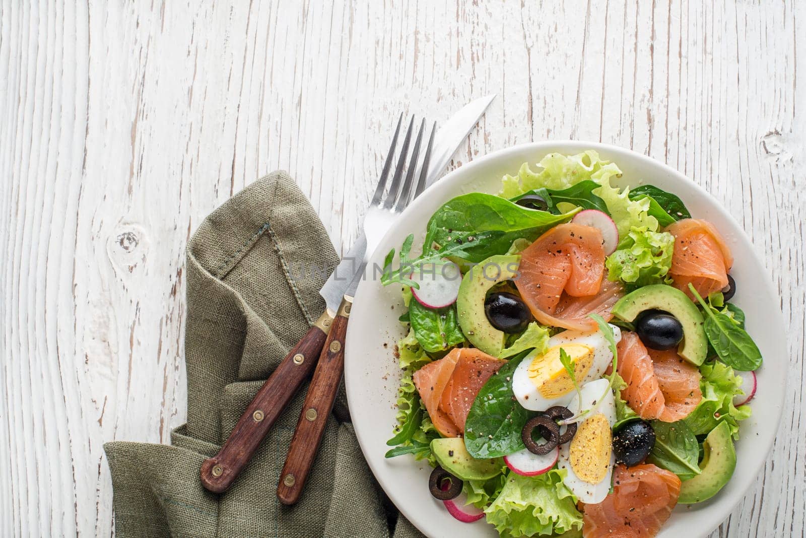 Fresh green lettuce salad with smoked salmon and avocado on wooden background