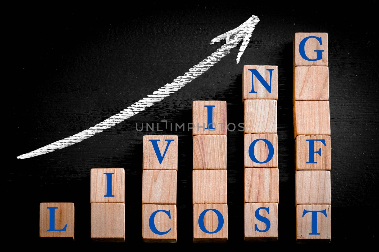 Message COST OF LIVING on ascending arrow above bar graph of Wooden small cubes isolated on black background. Chalk drawing on blackboard. Business Concept image.