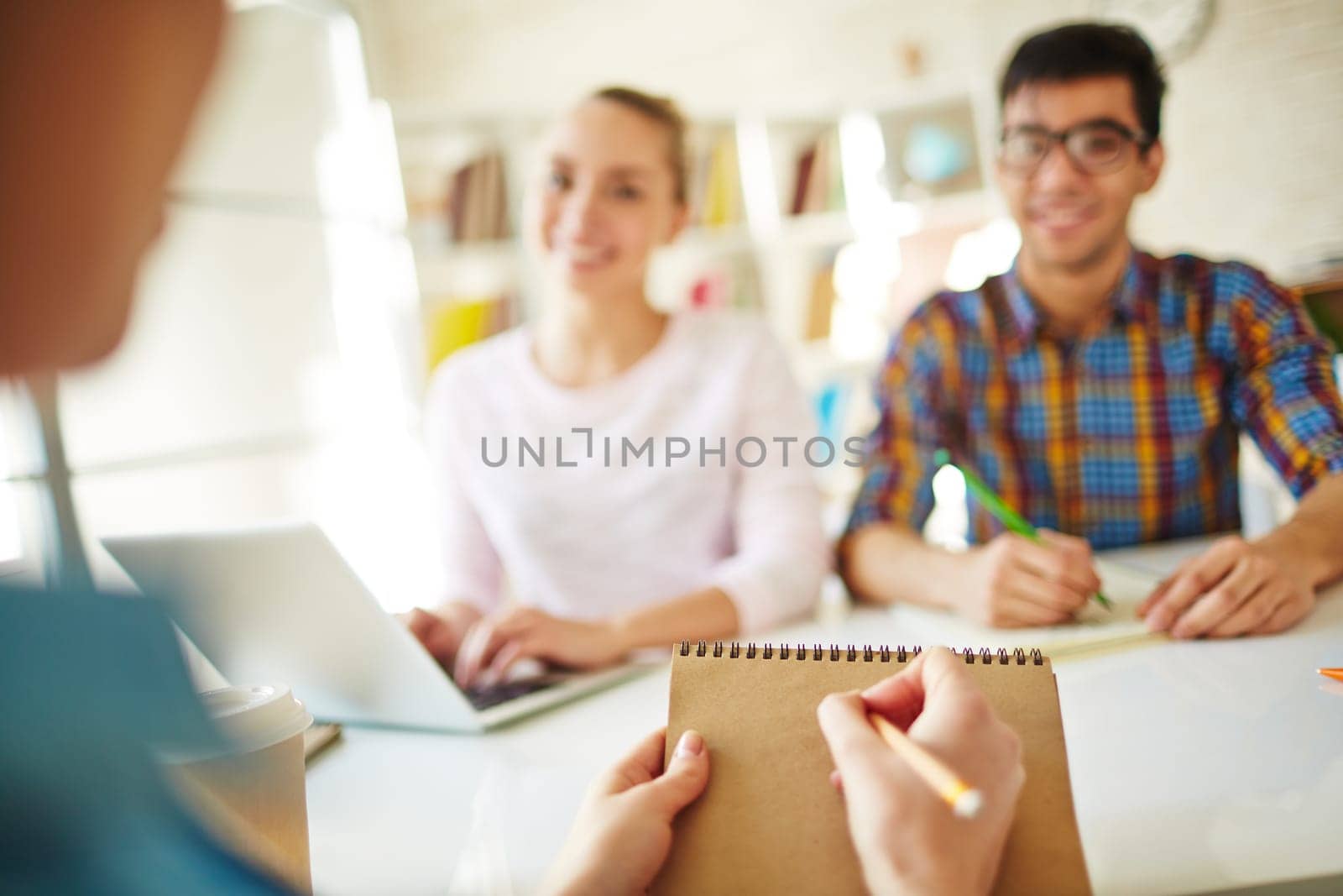 Student making notes in notepad with two groupmates in front