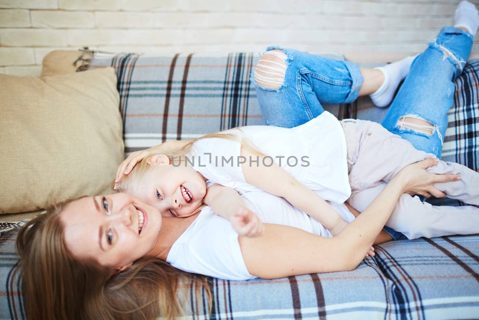 Happy little girl and her mother relaxing on sofa