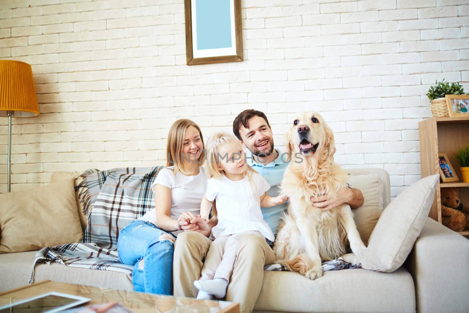 Cute little girl and her parents with dog resting on sofa at home