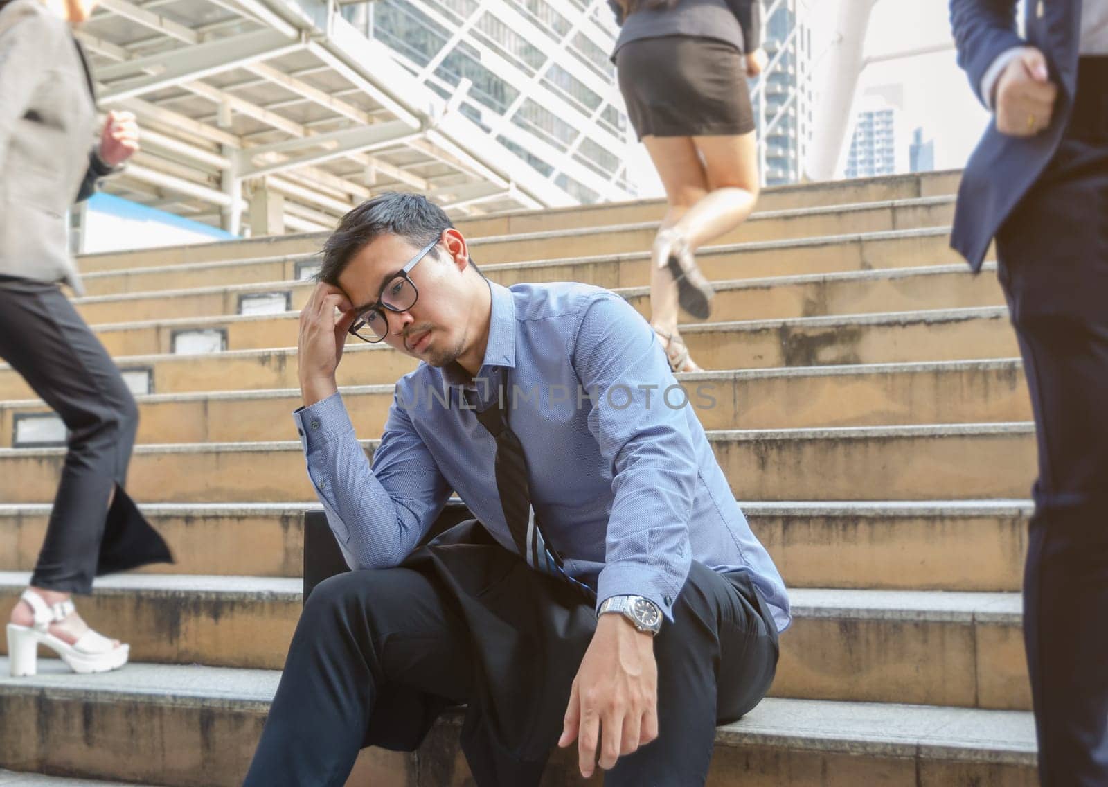 Depressed business man sitting still on busy stairs outdoors with blurry businesswomen walking past him in the city. Jobless man despair economic crisis, business failure or global economy recession