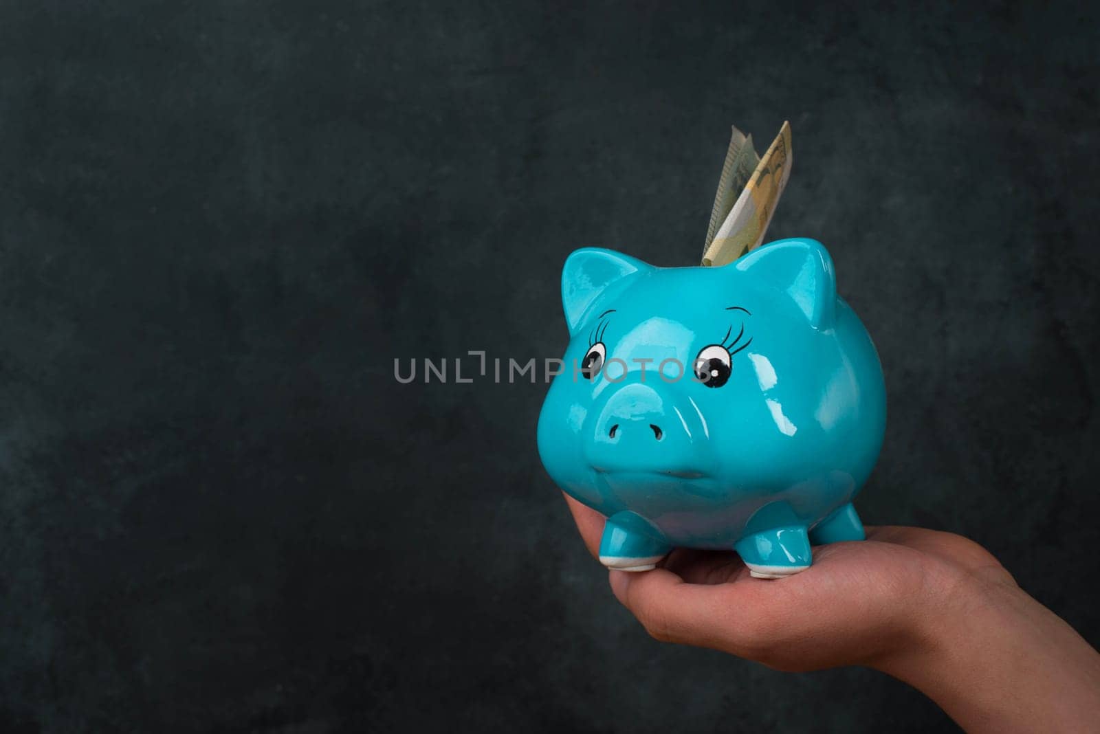 Putting money into a blue piggy bank, empty copy space for text