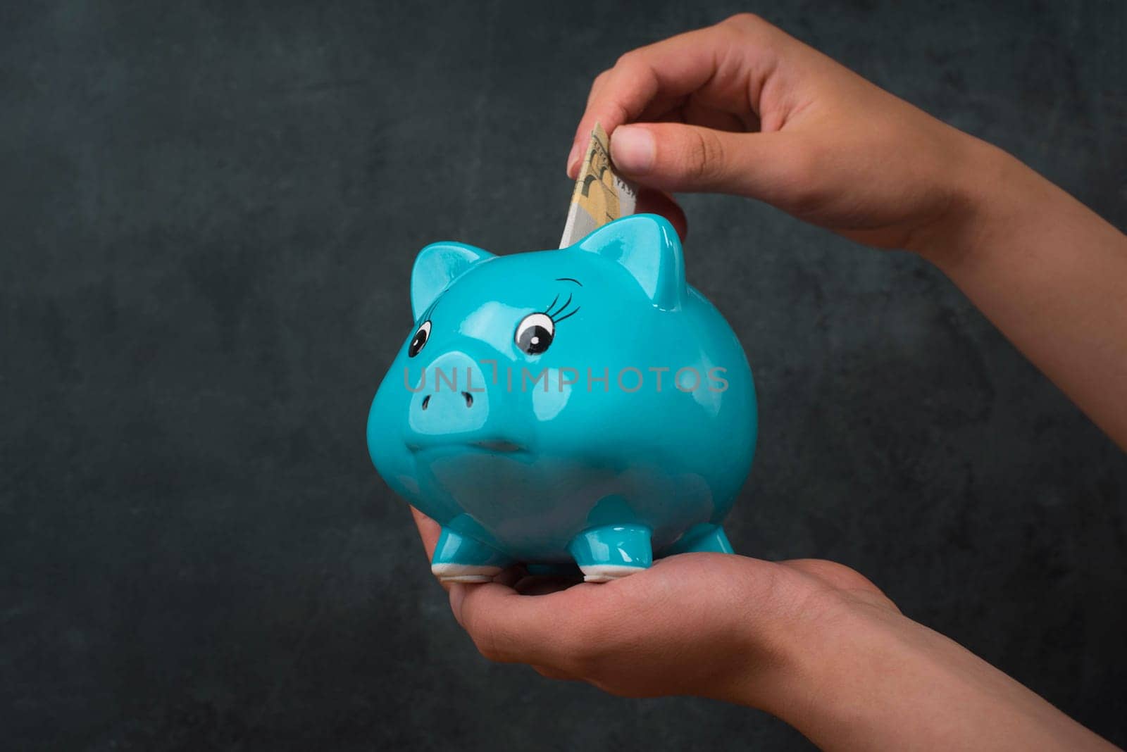 Putting money into a blue piggy bank, empty copy space for text