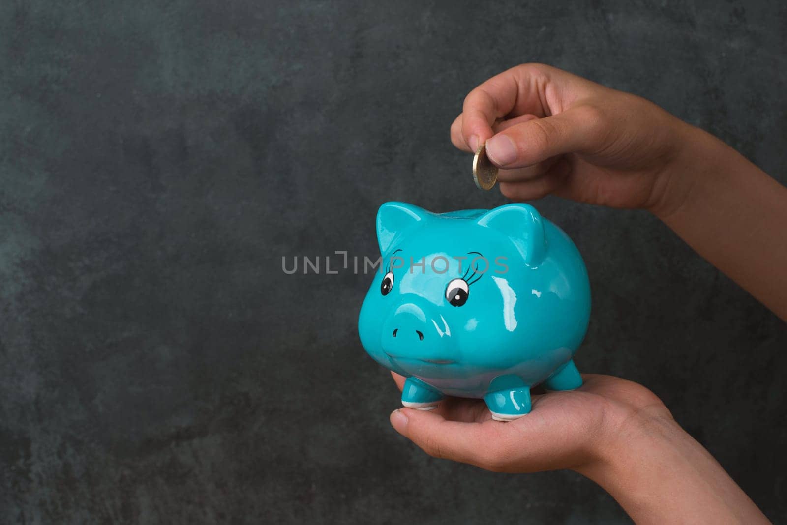 Putting money into a blue piggy bank, empty copy space for text