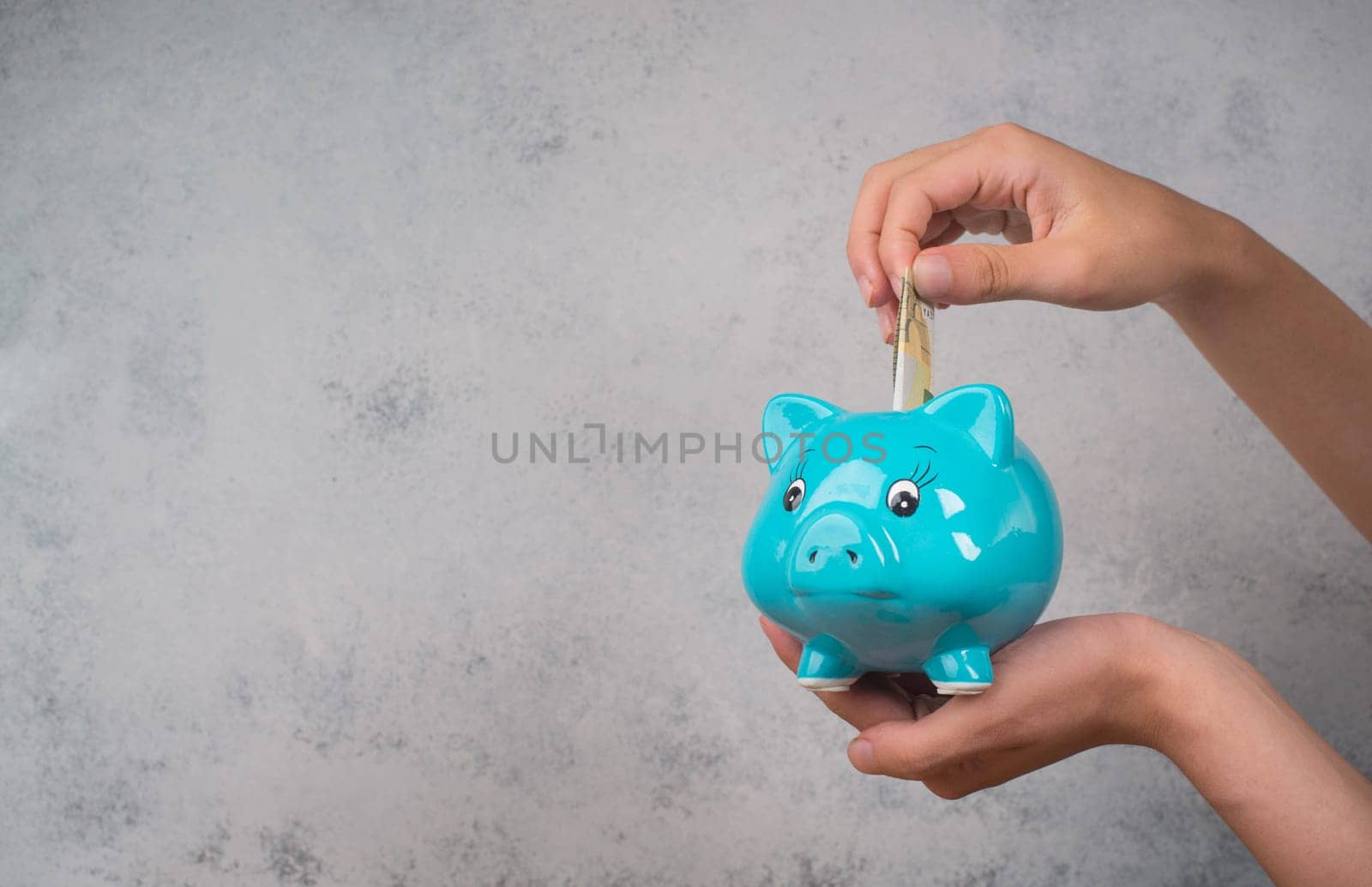 Putting money into a blue piggy bank, empty copy space for text
