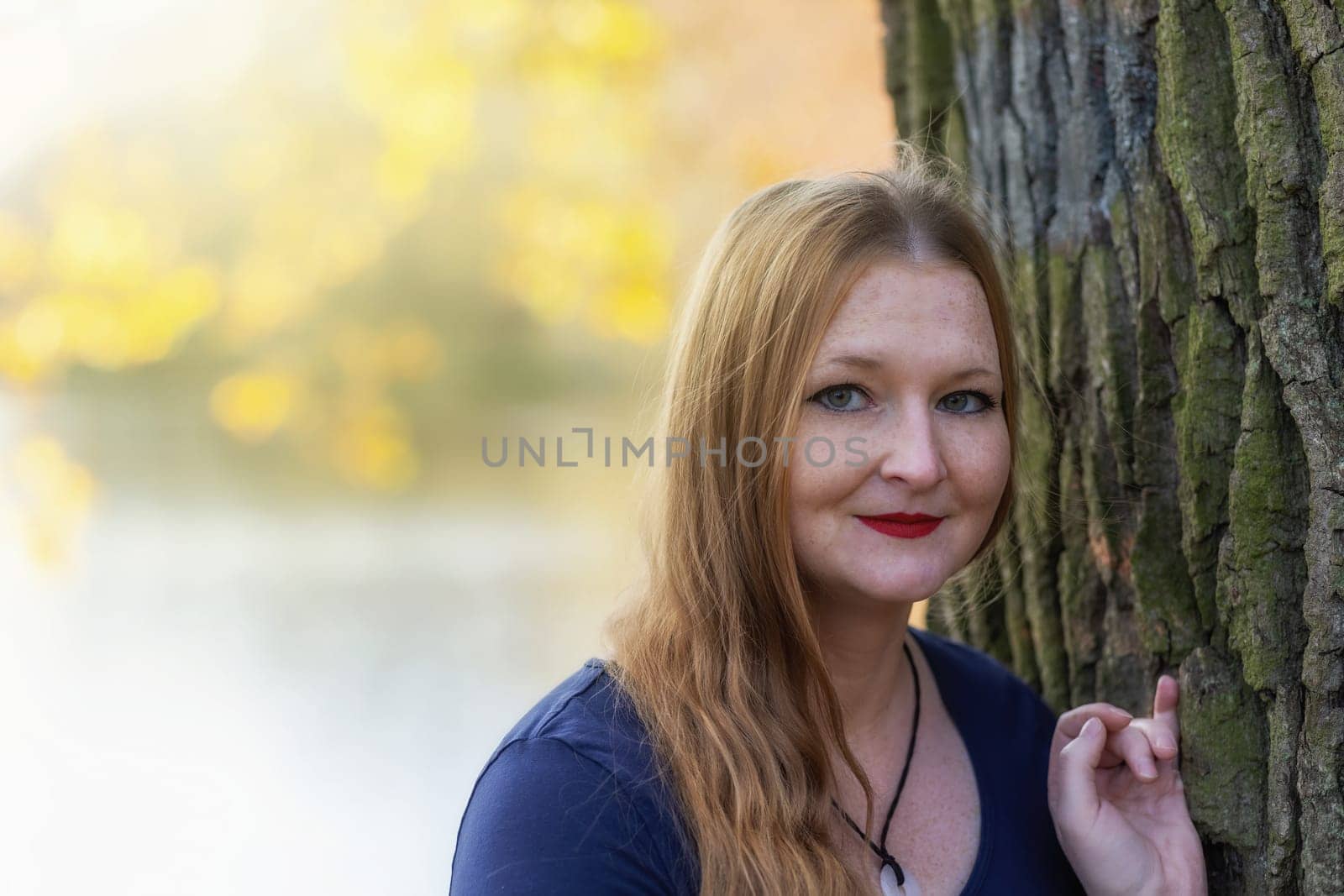Portrait of freckled young woman  with red lips is posing in autumn park. The woman is looking at the camera.