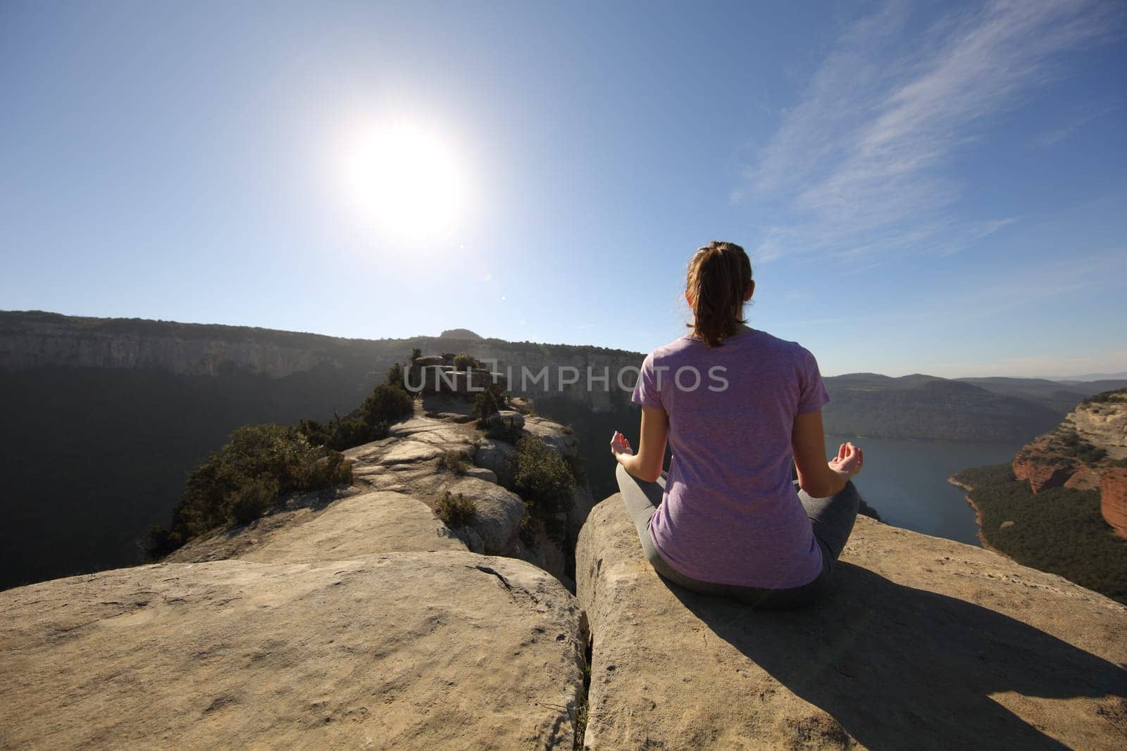 Back view portrait of a person doing yoga exercise in the top of a cliff in the mountain in front of the sun
