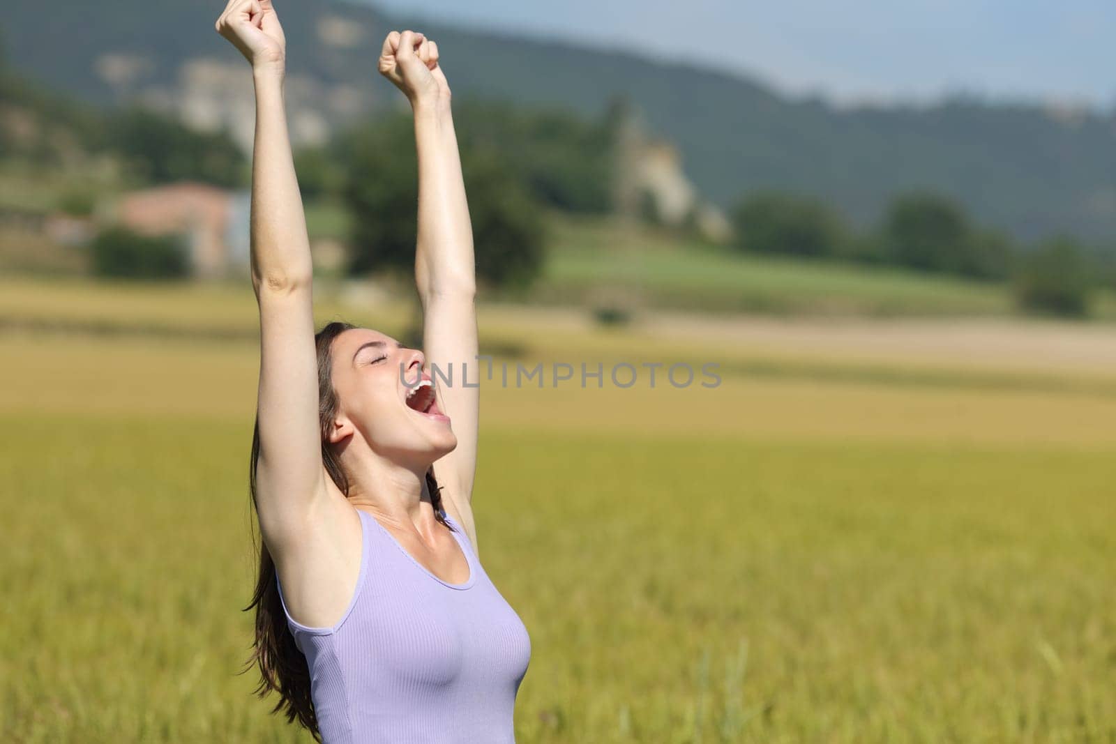 Excited woman raising arms and screaming celebrating summer vacation in a wheat field