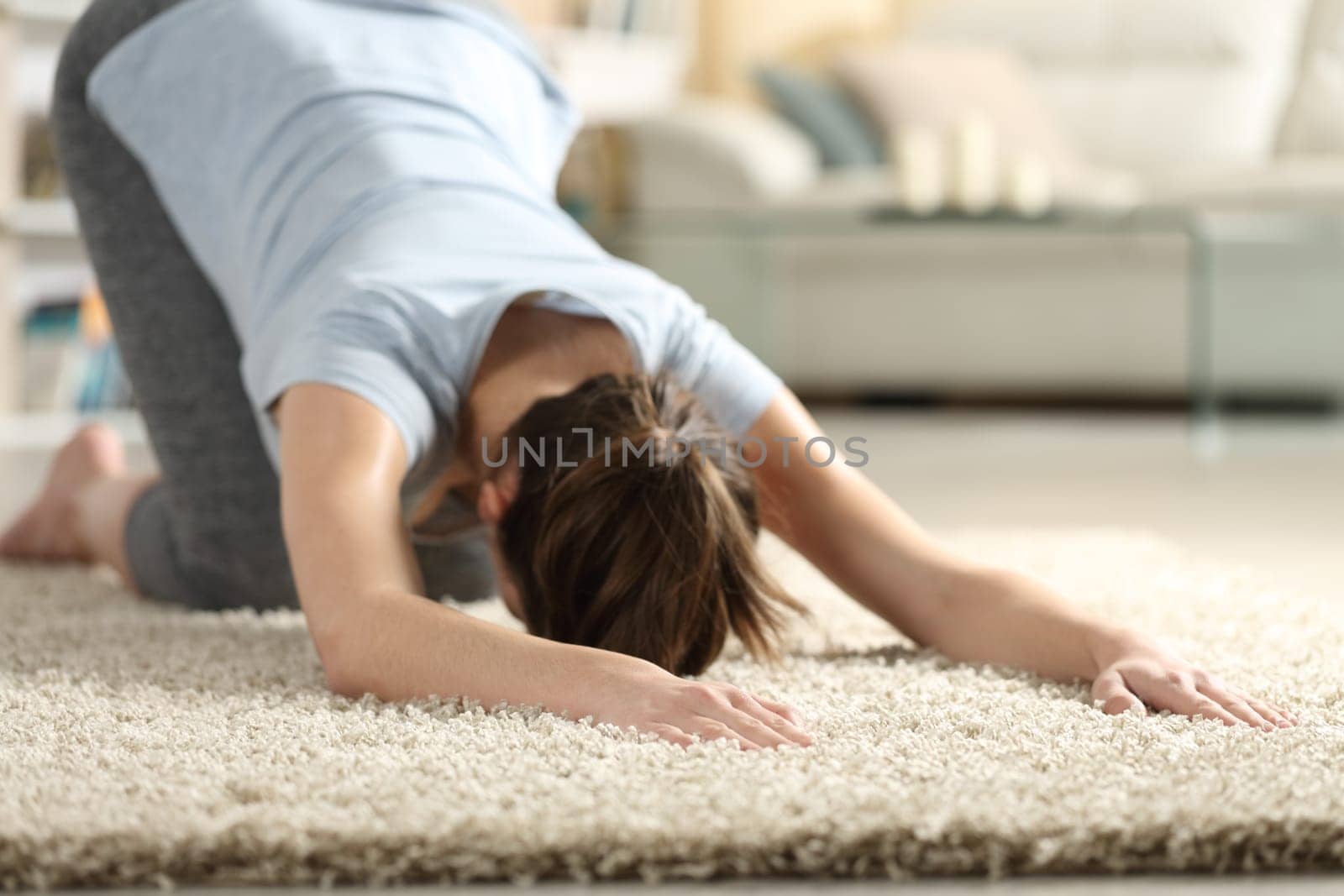 Female exercising yoga melting heart pose on a carpet in the living room at home