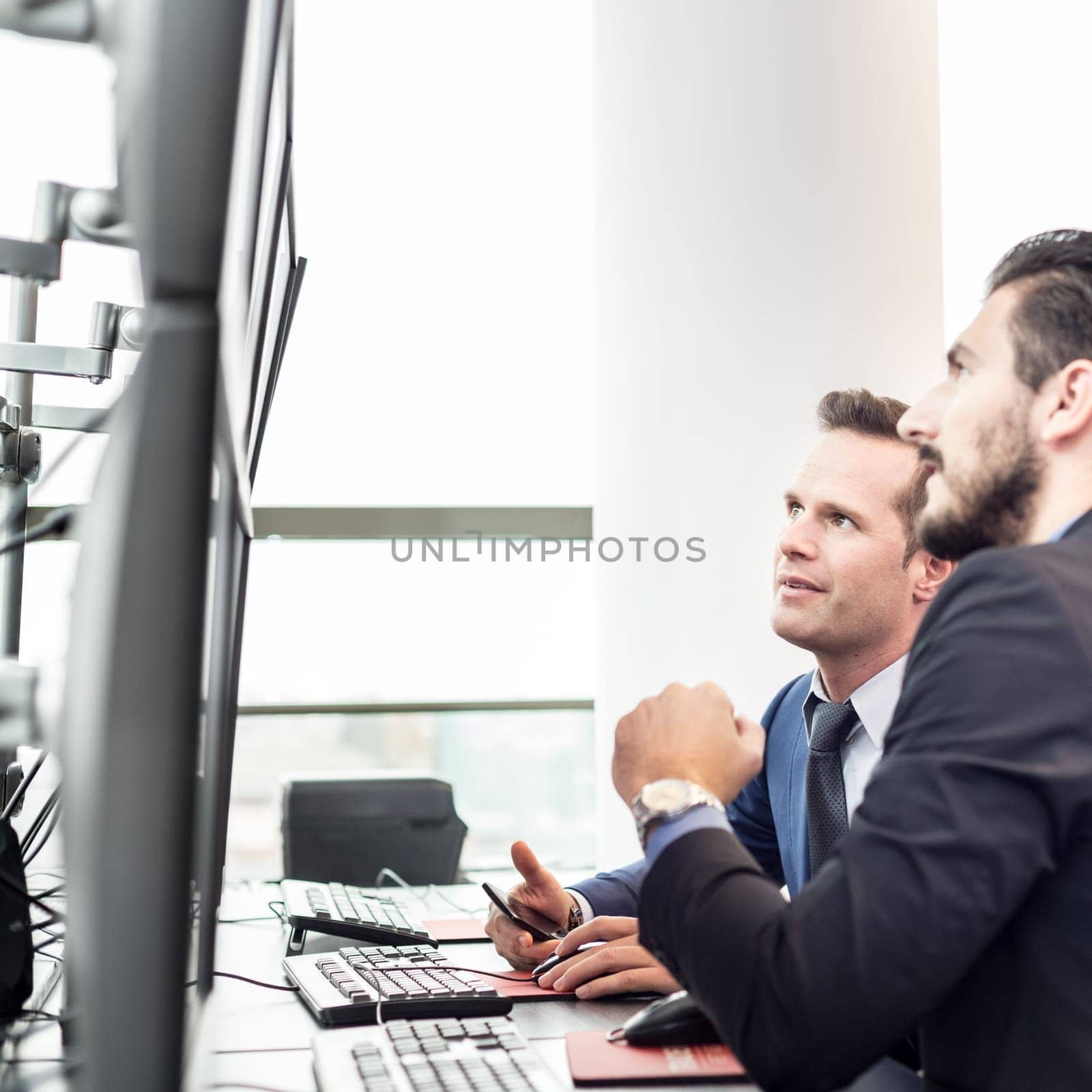 Successful businessmen trading stocks. Stock traders looking at graphs, indexes and numbers on multiple computer screens. Colleagues in traders office. Business success.