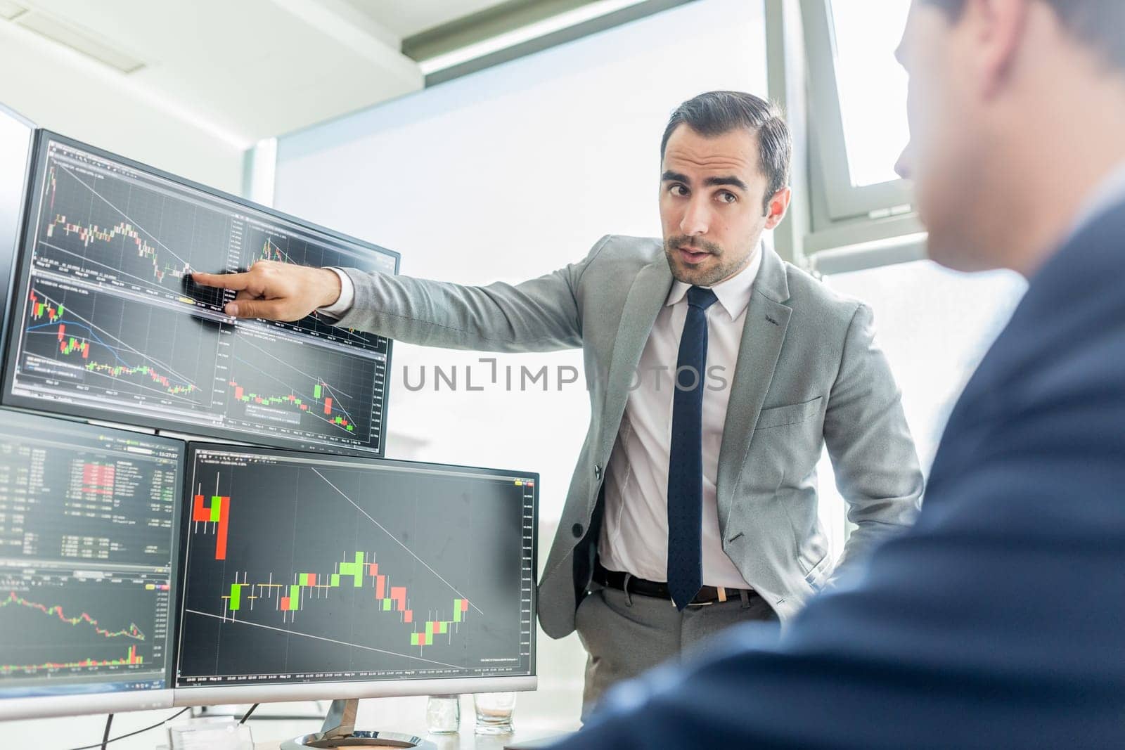 Businessmen trading stocks online. Stock brokers looking at graphs, indexes and numbers on multiple computer screens. Colleagues in discussion in traders office. Business success concept.