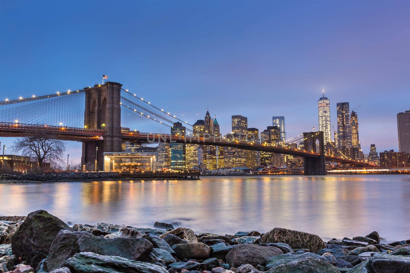 Brooklyn bridge and New York City Manhattan downtown skyline at dusk with skyscrapers illuminated over East River panorama.