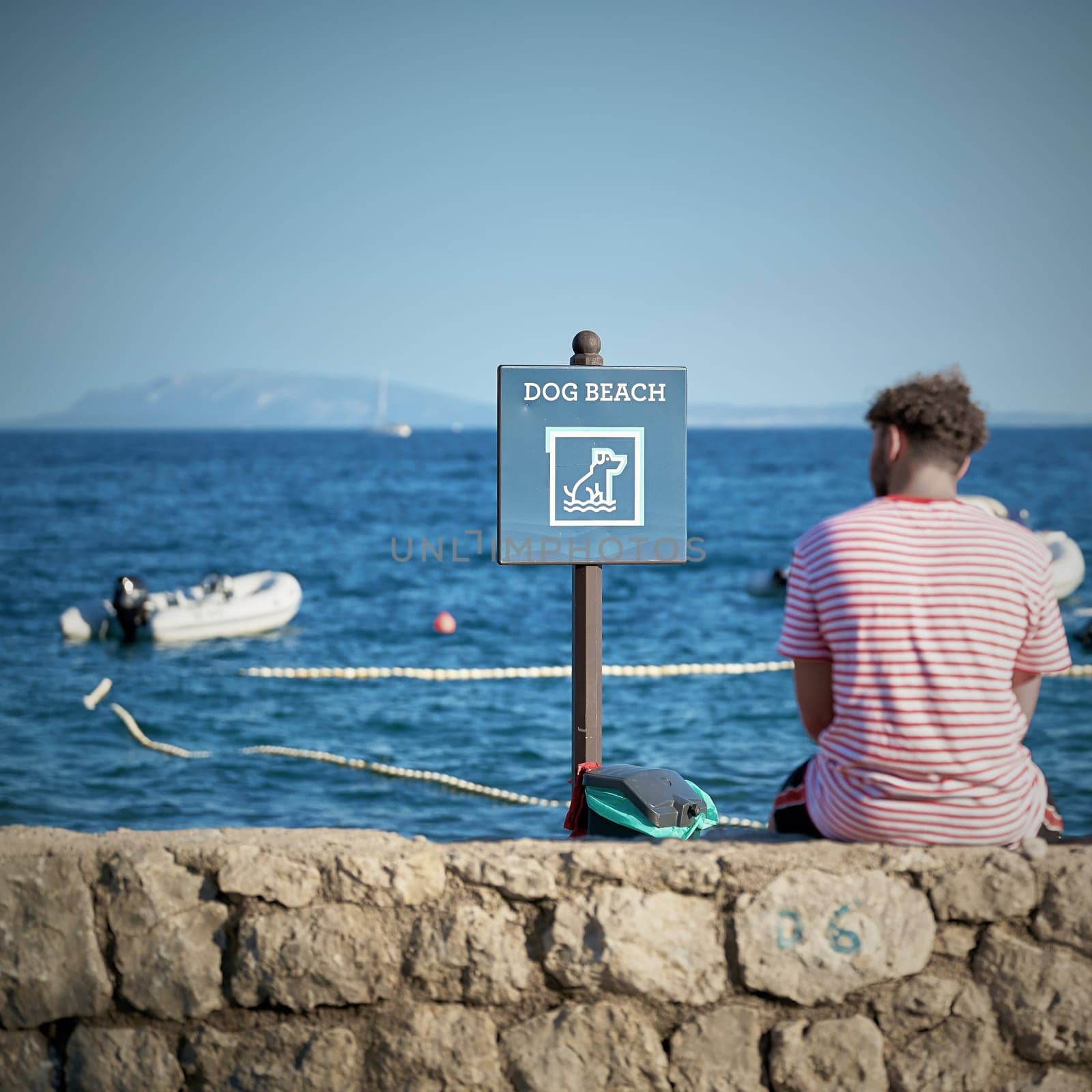 Sign with the inscription dog beach on a campsite in Krk in Croatia. Next to it a vacationer resting on a wall.